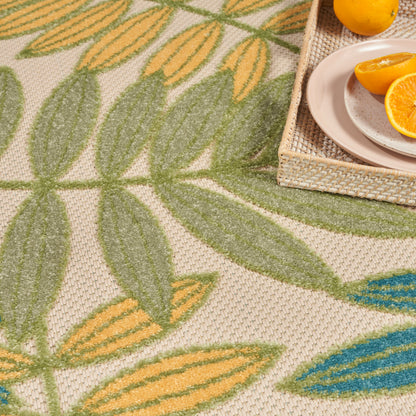 Beige woven rug with large green and yellow tropical leaf pattern; textured surface.