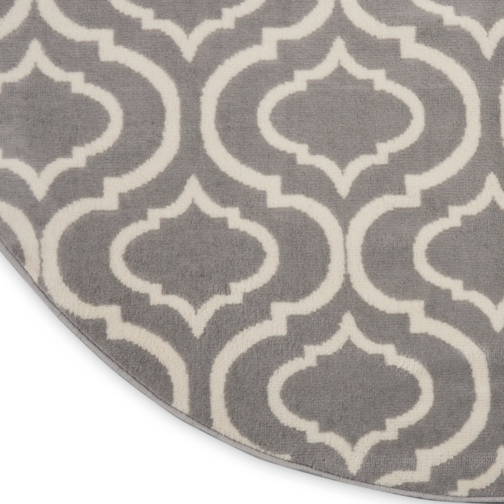 Grey round rug with a white quatrefoil lattice pattern.