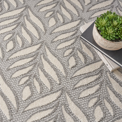 Gray and cream leaf-patterned woven rug; modern botanical design with a stack of books and a small potted succulent.