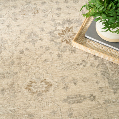 Beige oriental rug with subtle floral motif; light wicker tray holds a potted green fern and stacked books.