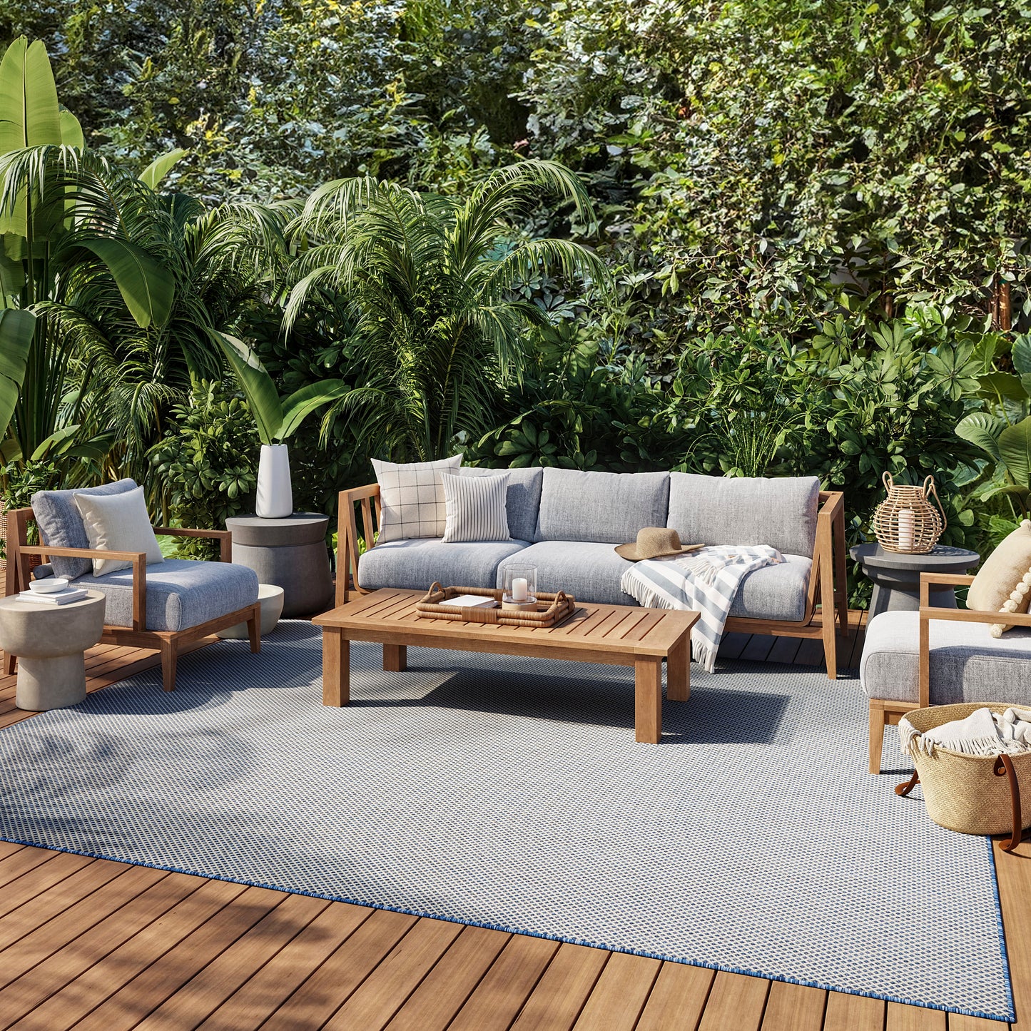 Outdoor lounge set with gray cushions and wooden frames, coffee table on a blue-gray rug amid tropical plants.