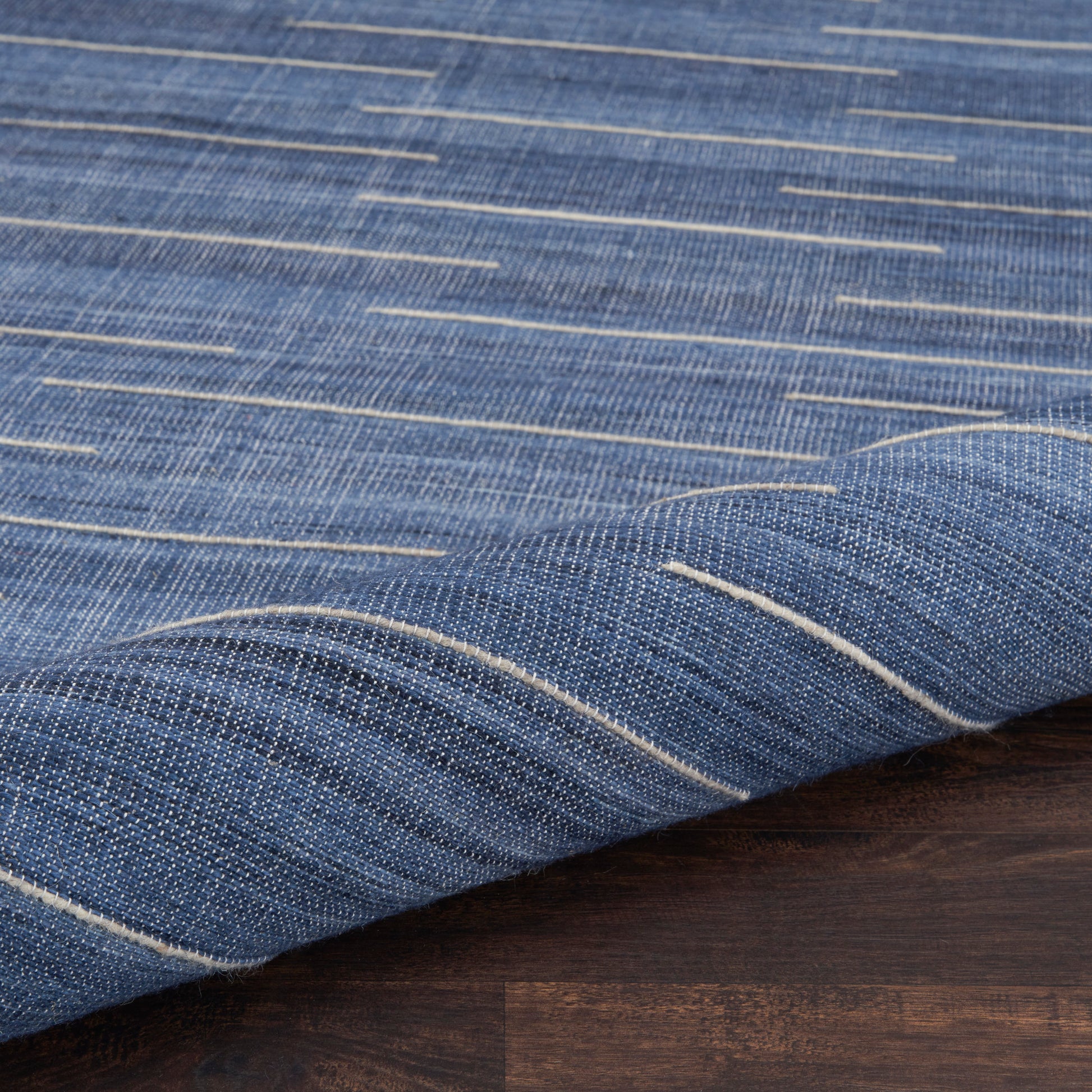 Blue denim-style woven rug with white stitch lines, folded over a dark wooden surface.