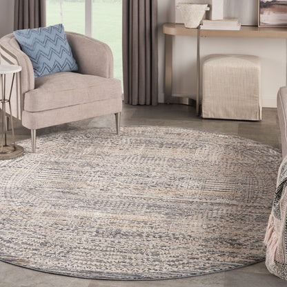 Round gray-beige patterned area rug under a beige upholstered armchair with a blue chevron pillow in a contemporary living room.
