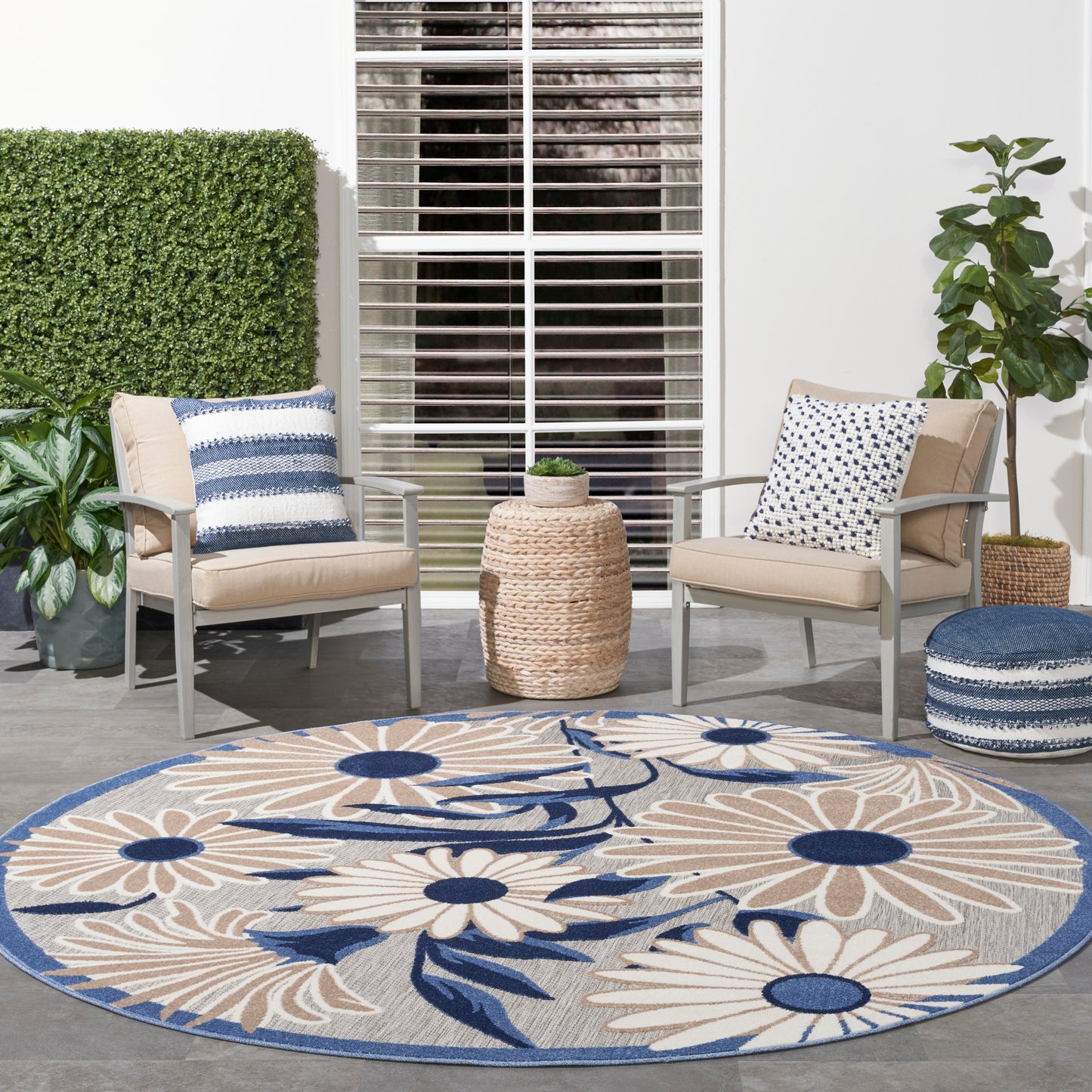 Outdoor patio with beige cushioned metal chairs, round woven rattan table, blue-striped pillows, and a large blue floral rug.