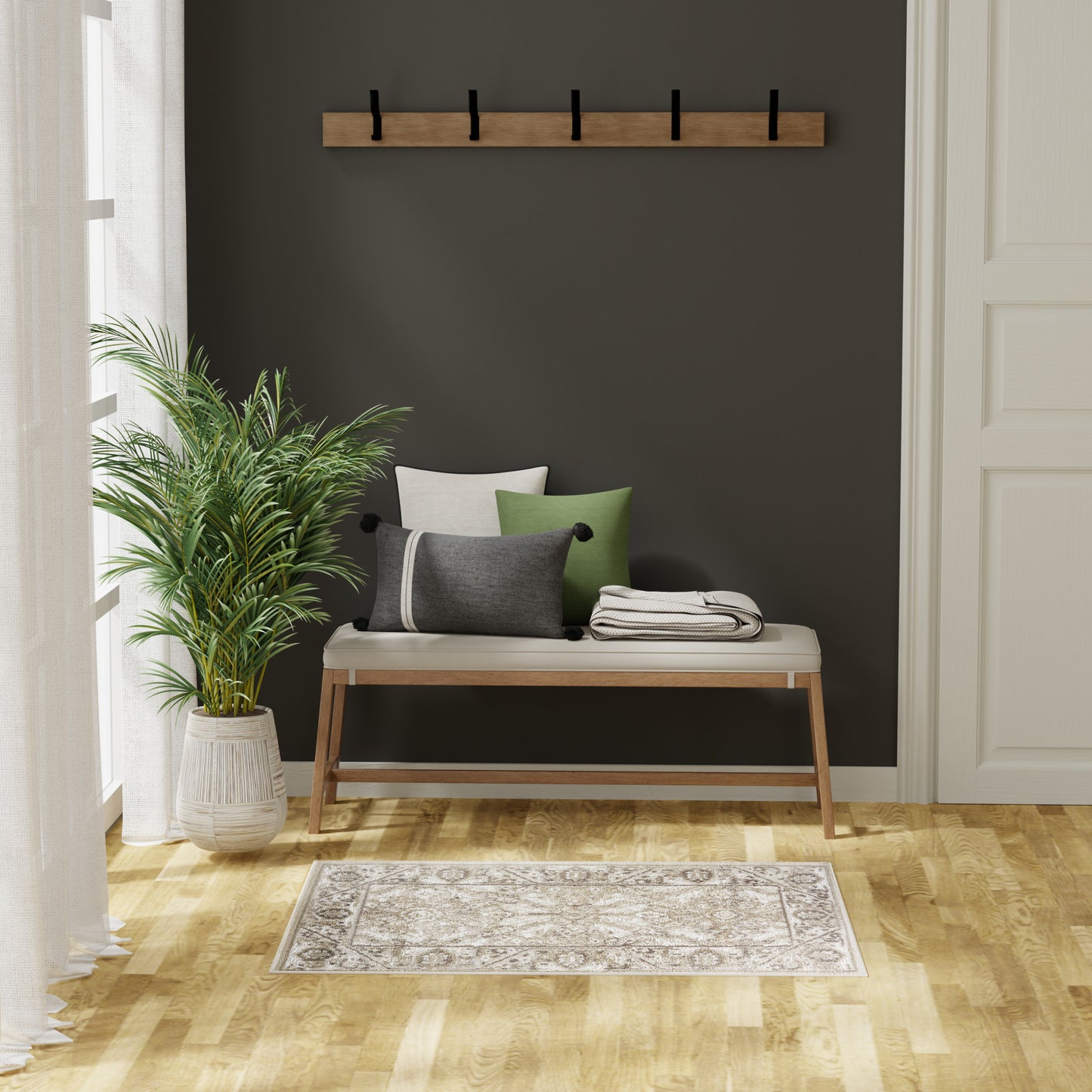 Wood-framed bench with light cushion and green/gray pillows against a dark wall, coat rack above, potted plant, beige patterned rug.