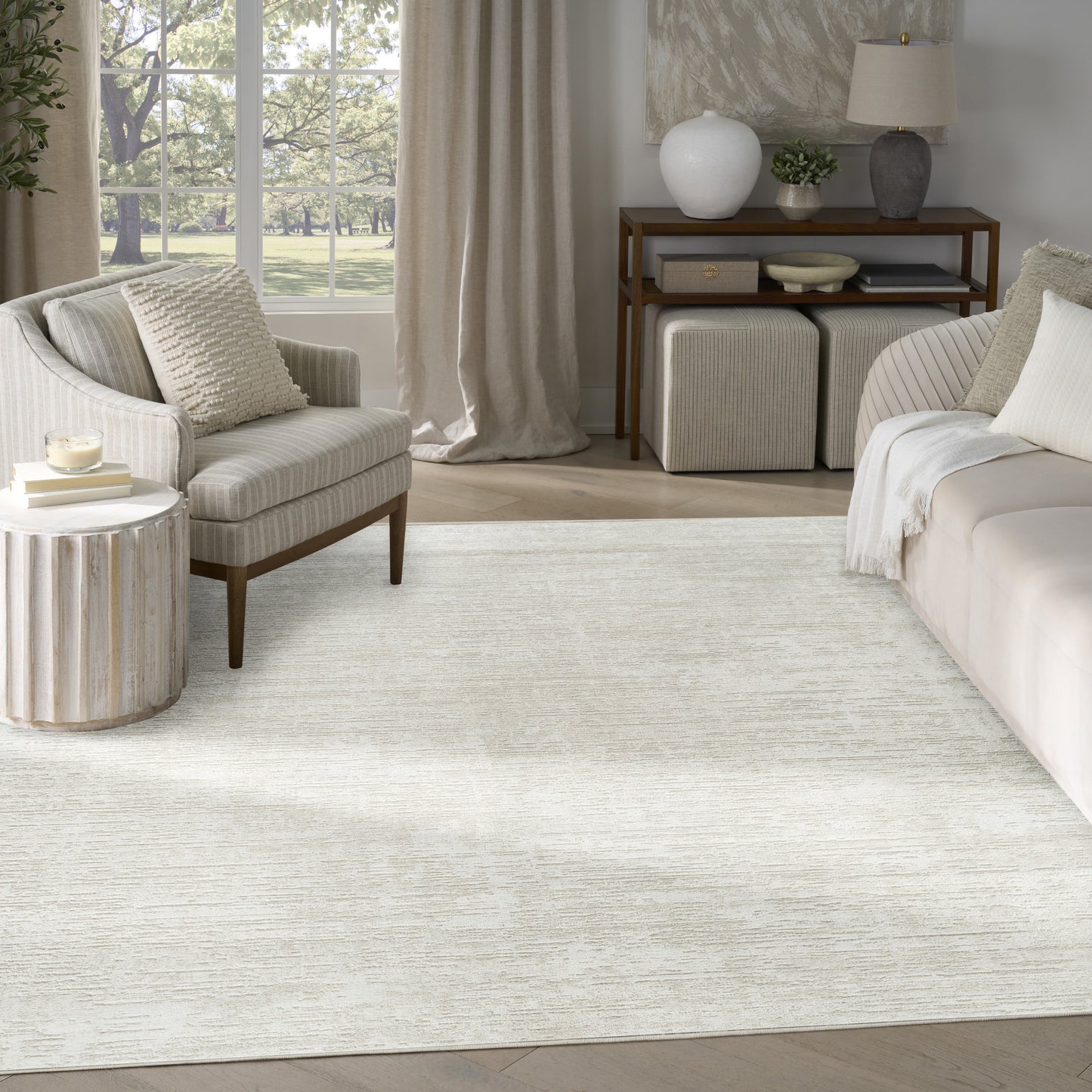 Soft, textured cream rectangular area rug in a neutral living room with beige sofa, armchair, and wooden console.