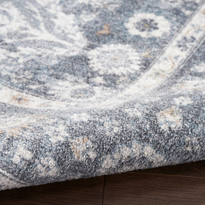 Soft blue and ivory patterned rug with a distressed medallion design, folded corner on dark wood floor.