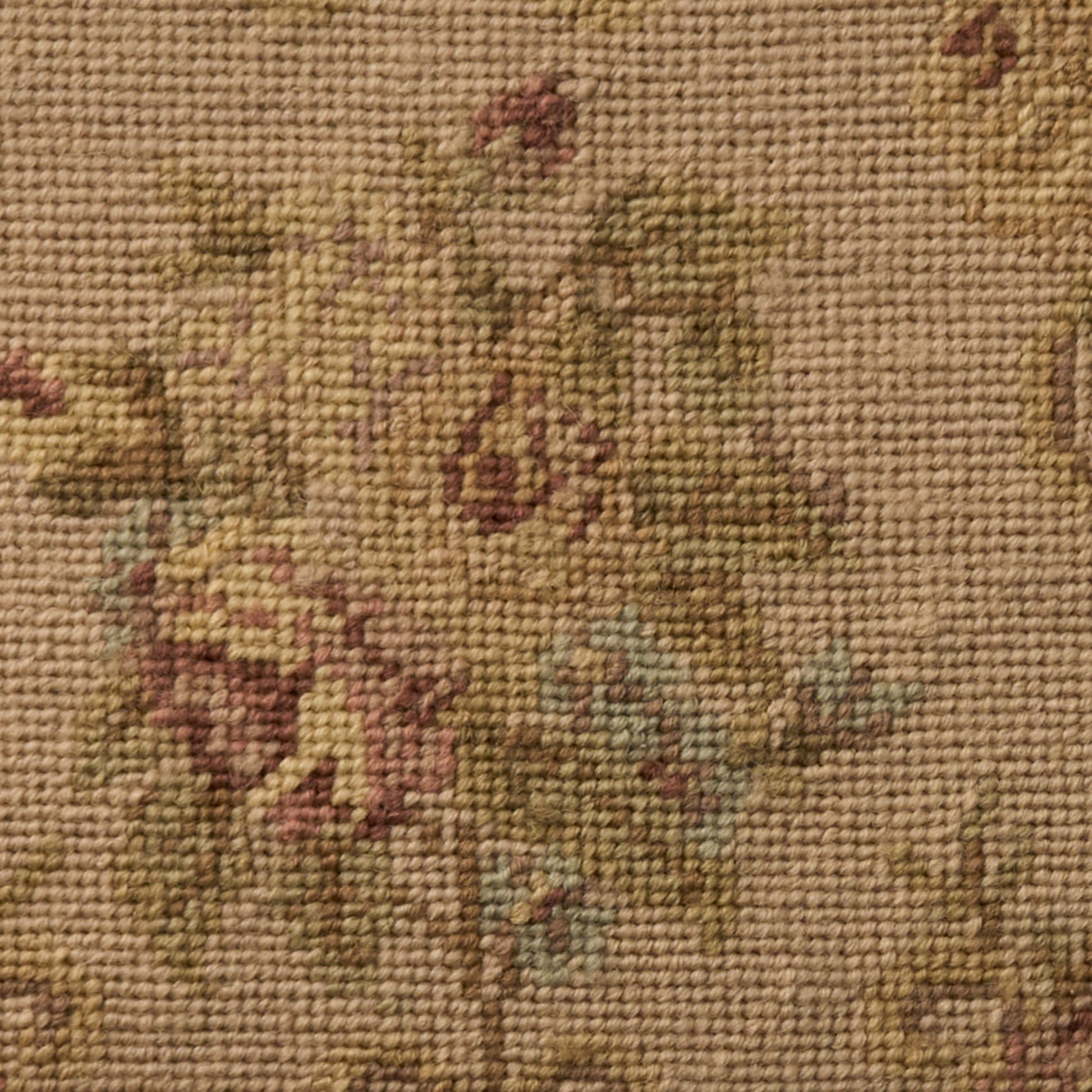 Close-up of a beige traditional floral woven rug with pink, green and blue accents and a textured pile.