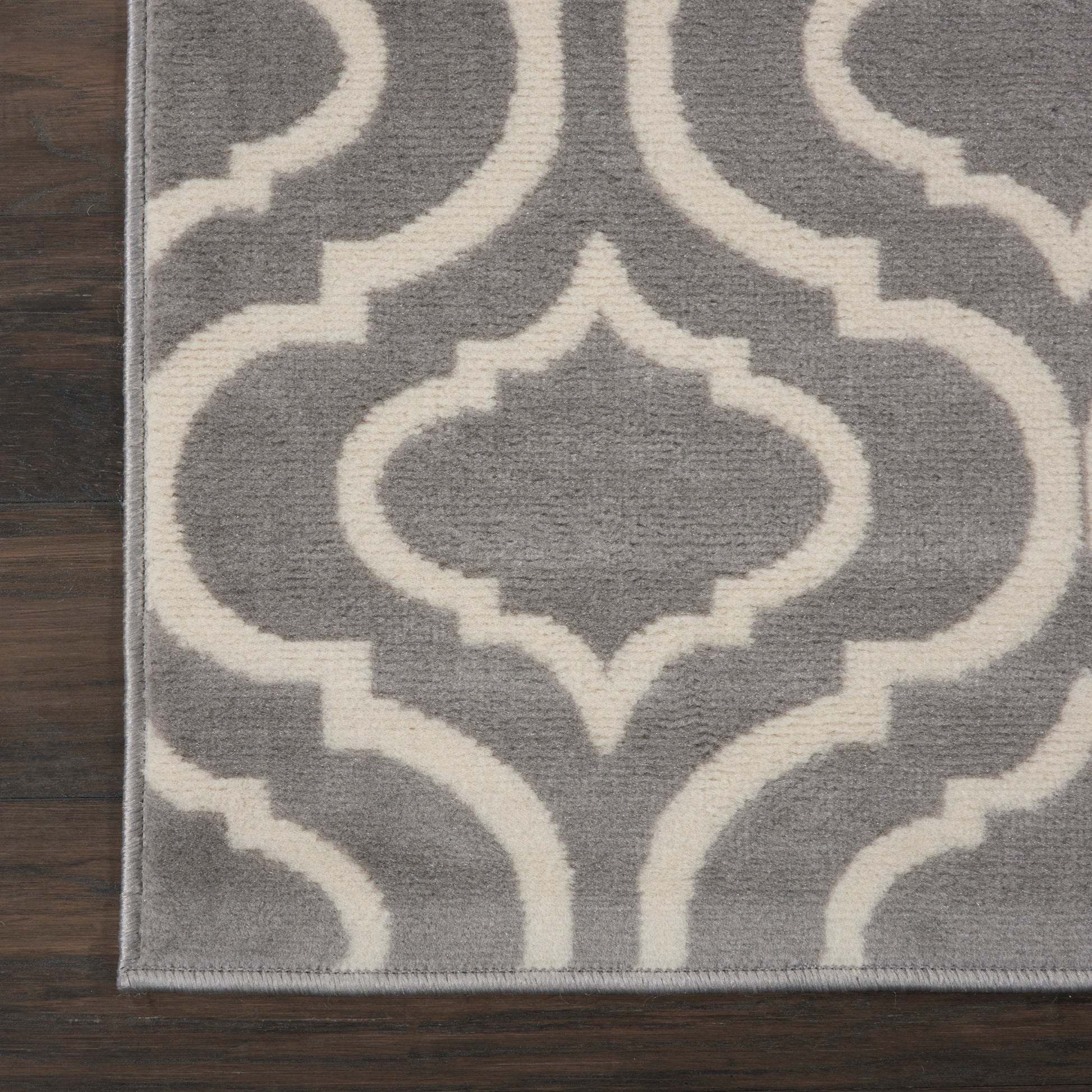 Gray rug with white geometric quatrefoil motif on dark wooden floor.