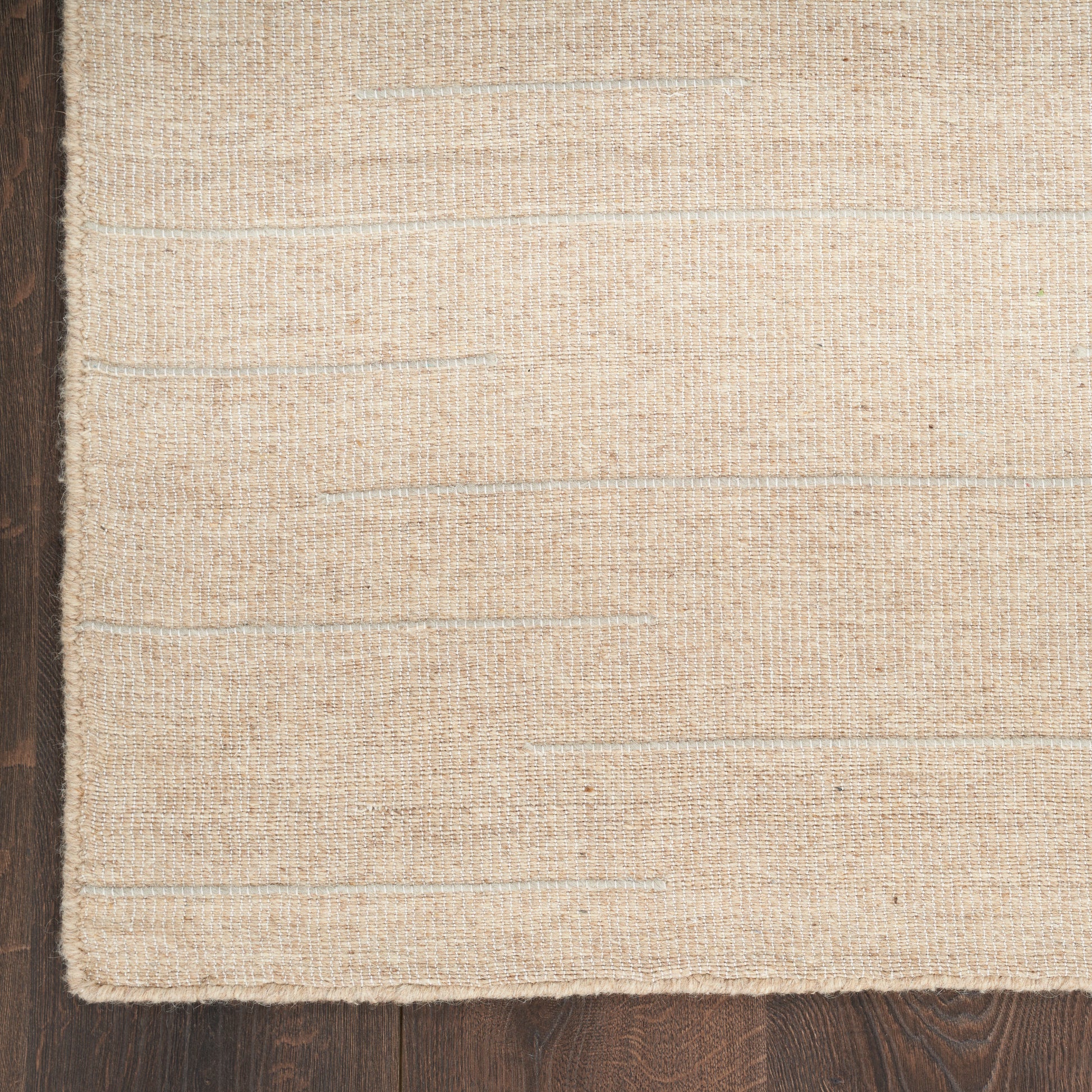 Beige woven rug with subtle horizontal texture on dark wooden floor.