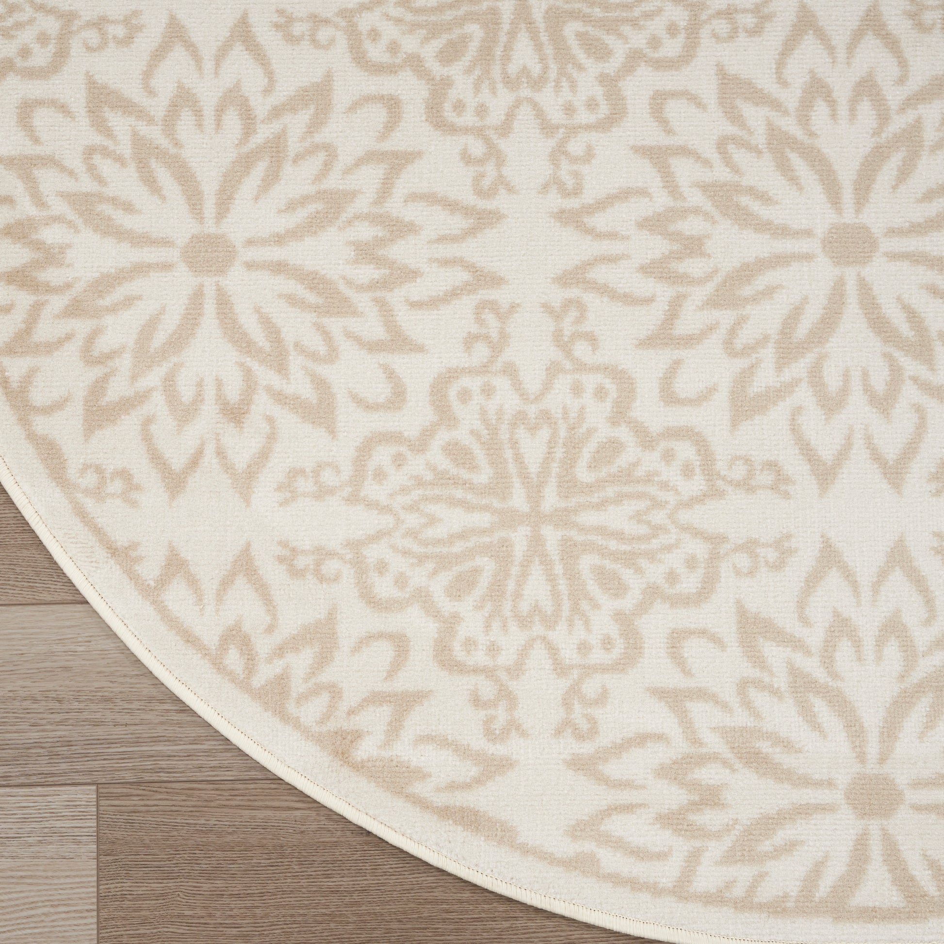 Round rug with cream background and beige damask floral pattern, woven texture on wood floor.