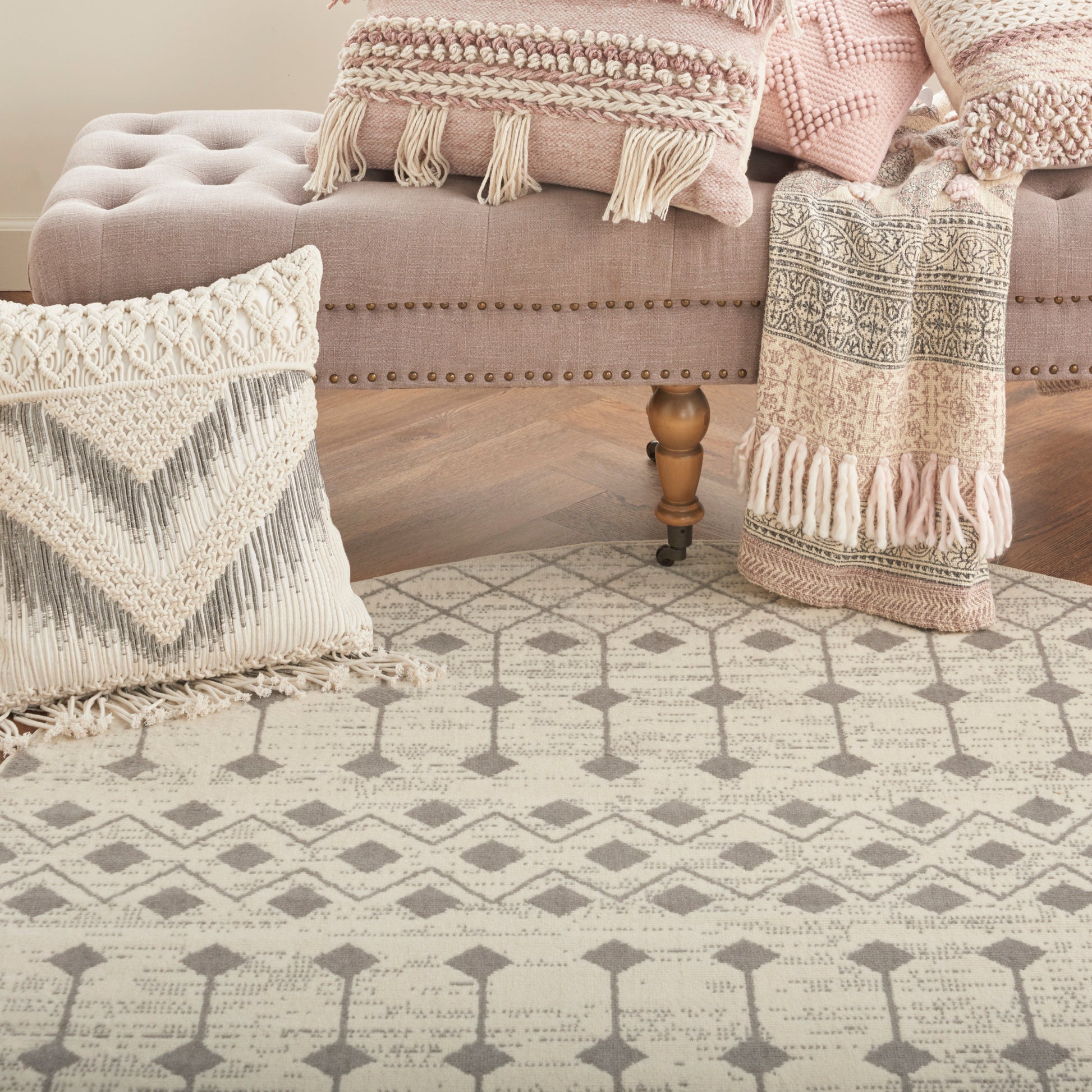 Boho chic living room scene with a tufted beige-pink sofa, fringed knit throws, decorative pillow, and a round geometric gray rug.