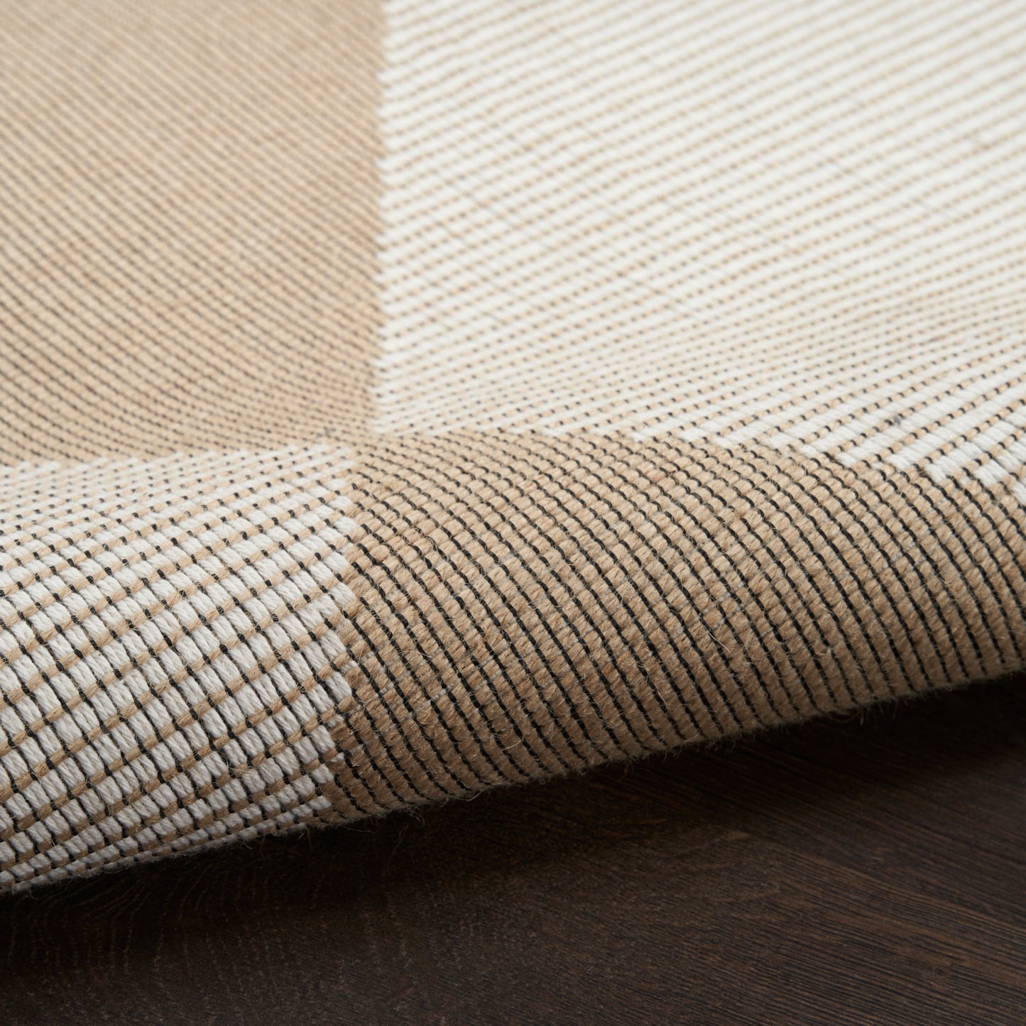 Beige, cream & tan woven checkered rug with fine brown stripes, rolled edge on dark wood floor.
