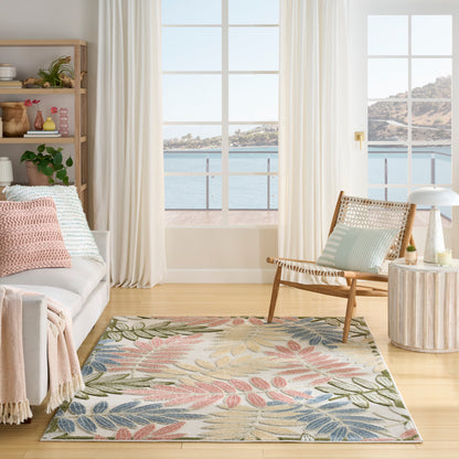 Pastel leaf-pattern area rug on light wood floor in a coastal living room with a rattan chair and sea view.