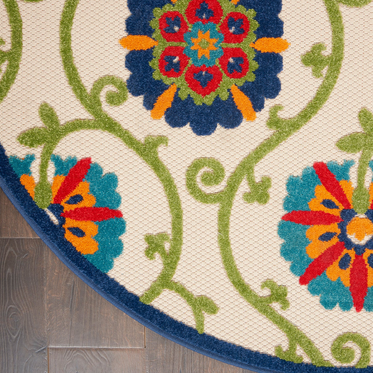 Close-up of a decorative rug with cream background, green vines, blue floral mandala, and multicolor petals; navy border.