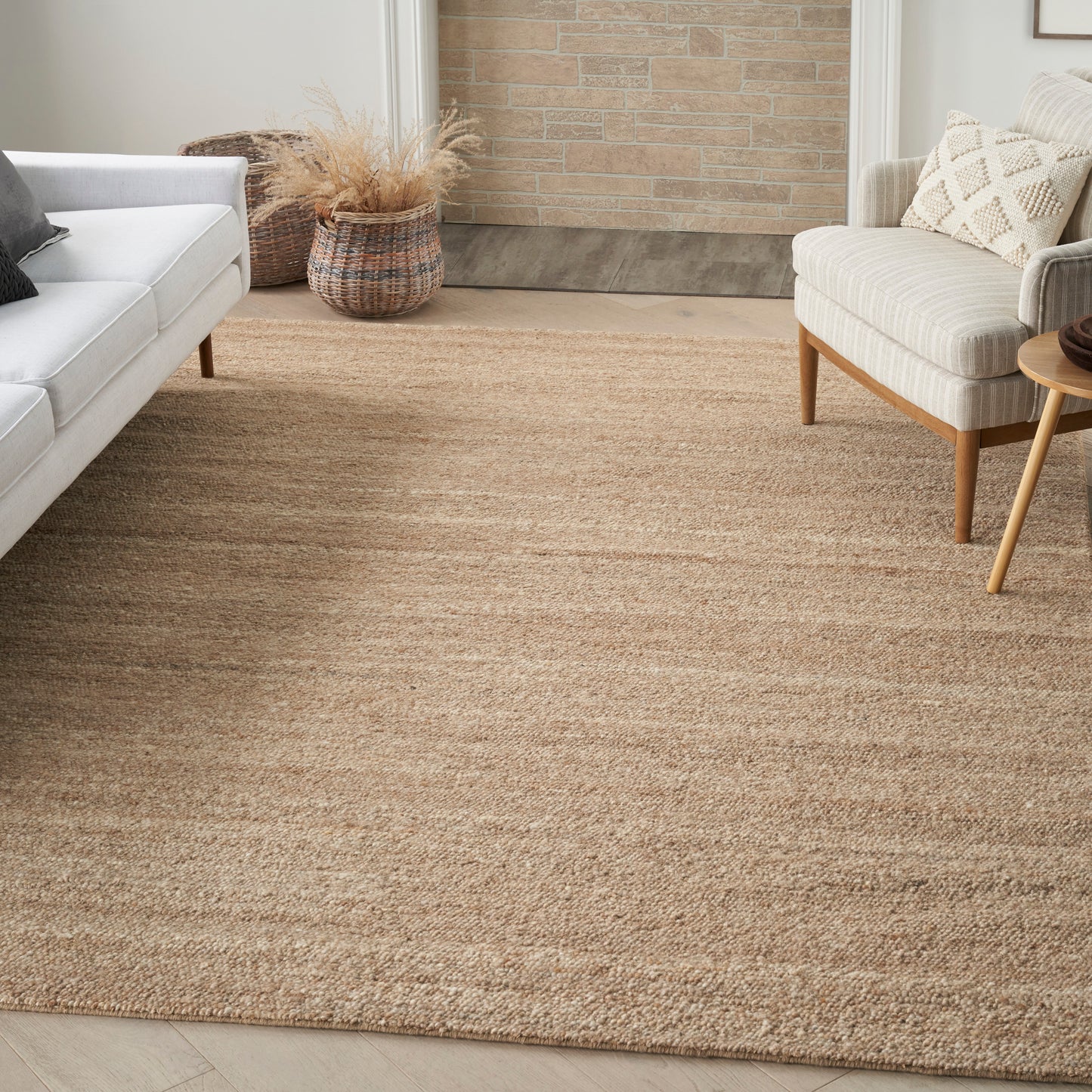 Natural jute area rug in a cozy living room with a light gray sofa, beige armchair, pampas grass basket & wooden accents.