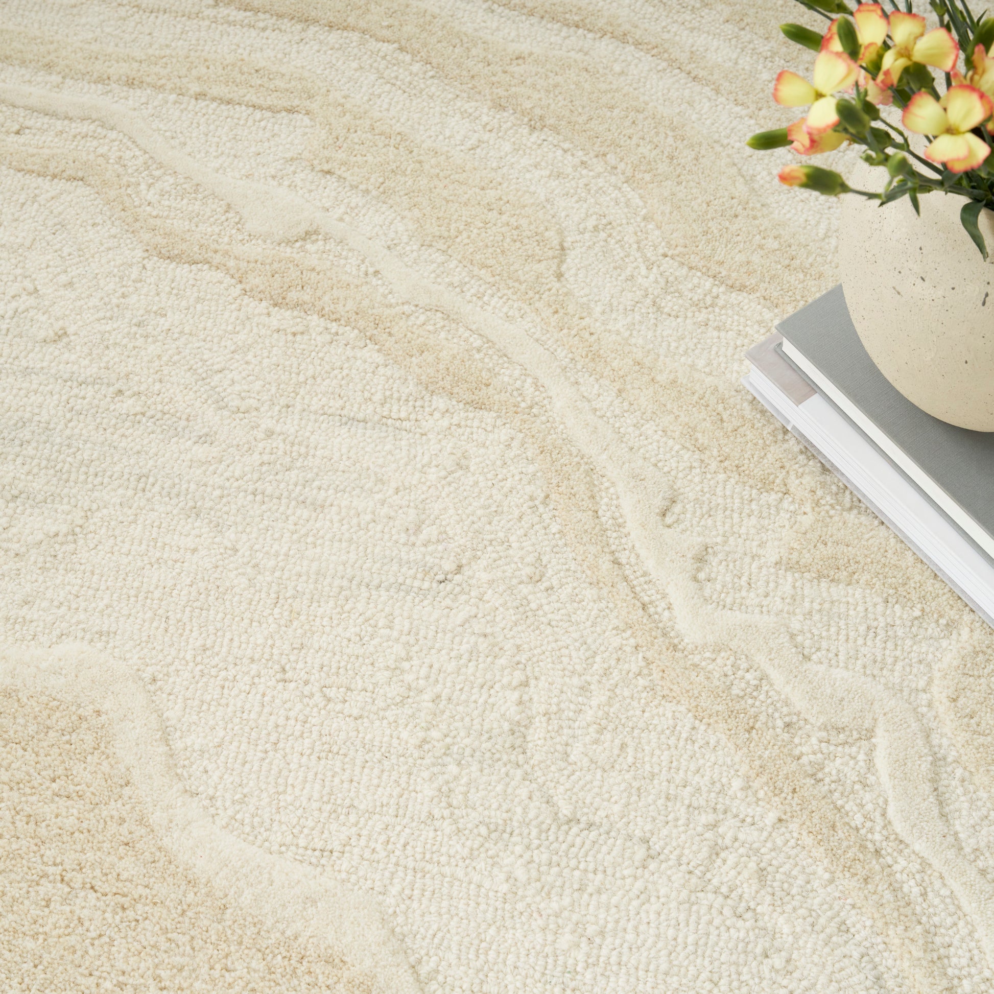 Beige textured rug with wavy patterns, plus a ceramic pot of orange flowers and a stack of books in the corner.