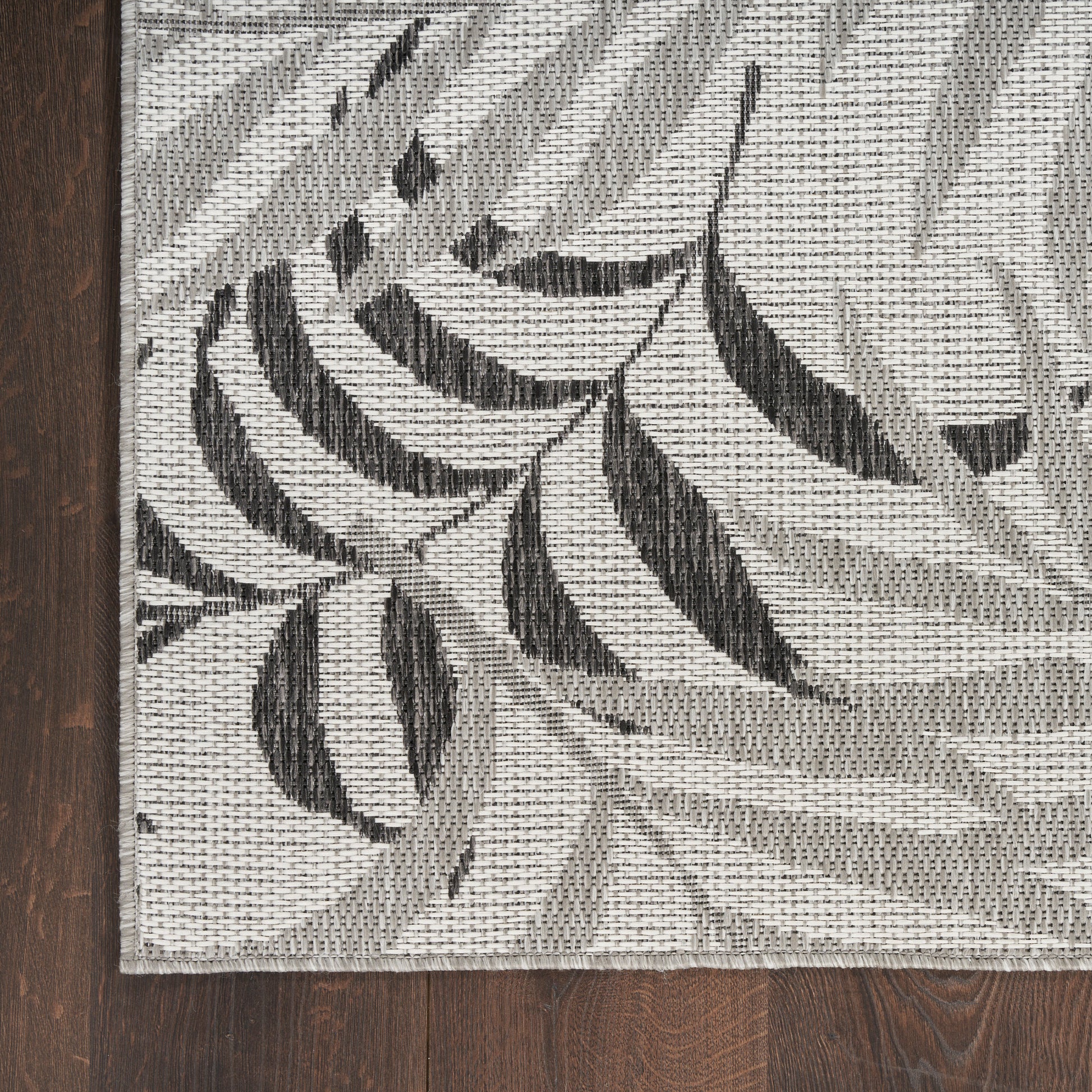 Botanical-patterned woven 8' runner rug in gray with charcoal leaf motifs on a light background, laid on dark wood floor.