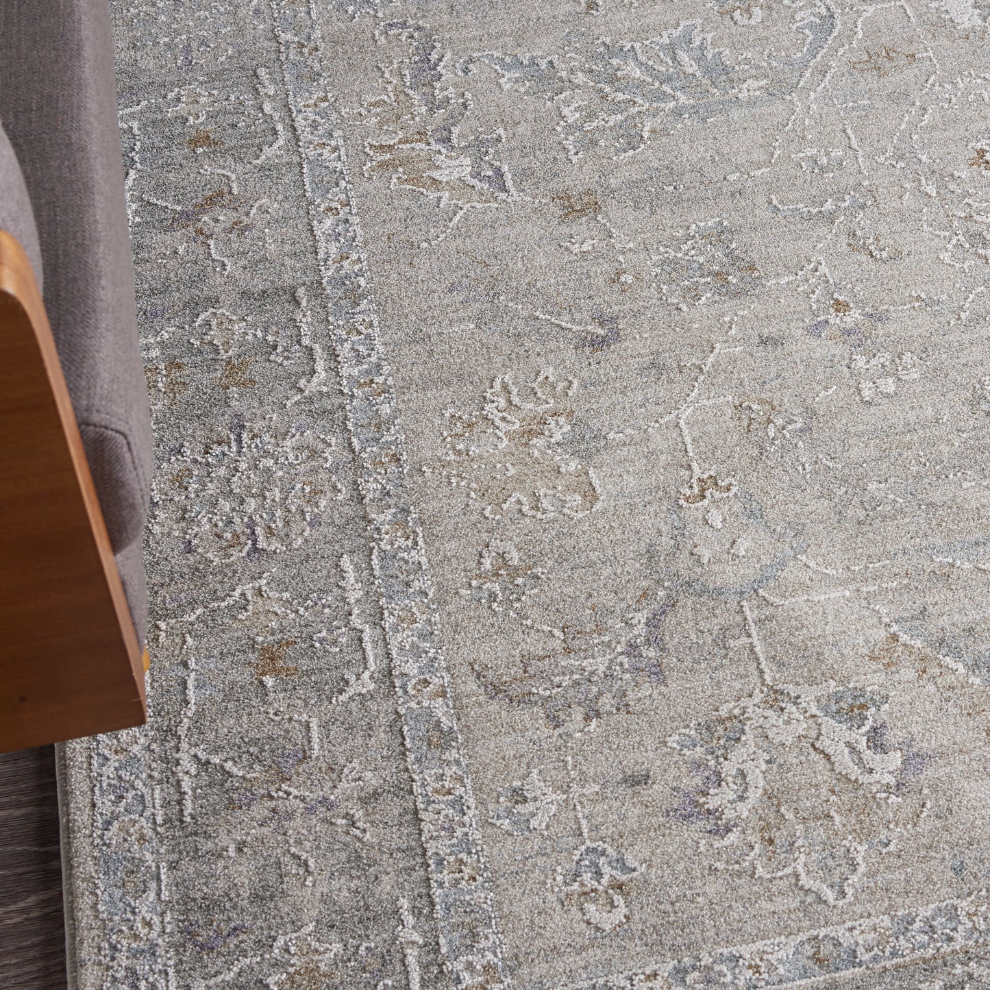 Gray antique-style area rug with pale blue floral motifs and a textured border beside a wooden chair.