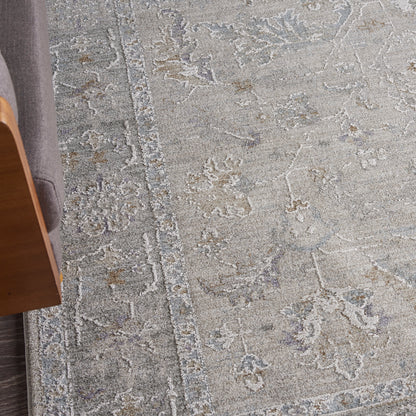 Gray antique-style area rug with pale blue floral motifs and a textured border beside a wooden chair.
