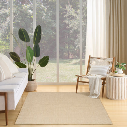 Bright living room with large windows, beige woven rug, white sofa, cane chair, and potted plant.