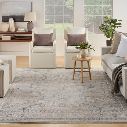 Gray patterned rug in a neutral living room with cream armchairs, a beige sofa and a round wood side table.