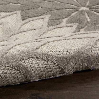 Beige and gray patterned plush rug with subtle leaf motif, folded edge on dark wood floor.