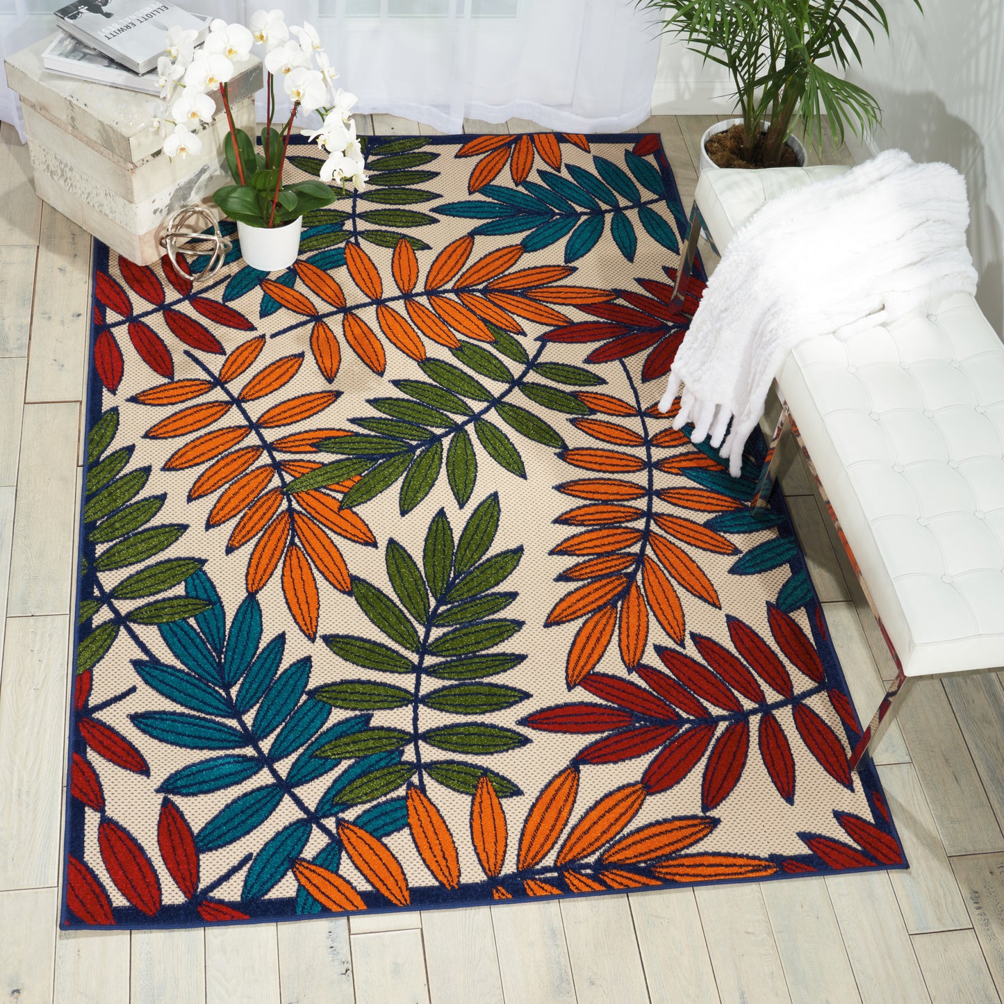 Rectangular area rug with bold multicolor leaf pattern in orange, teal, blue, green and red on beige.