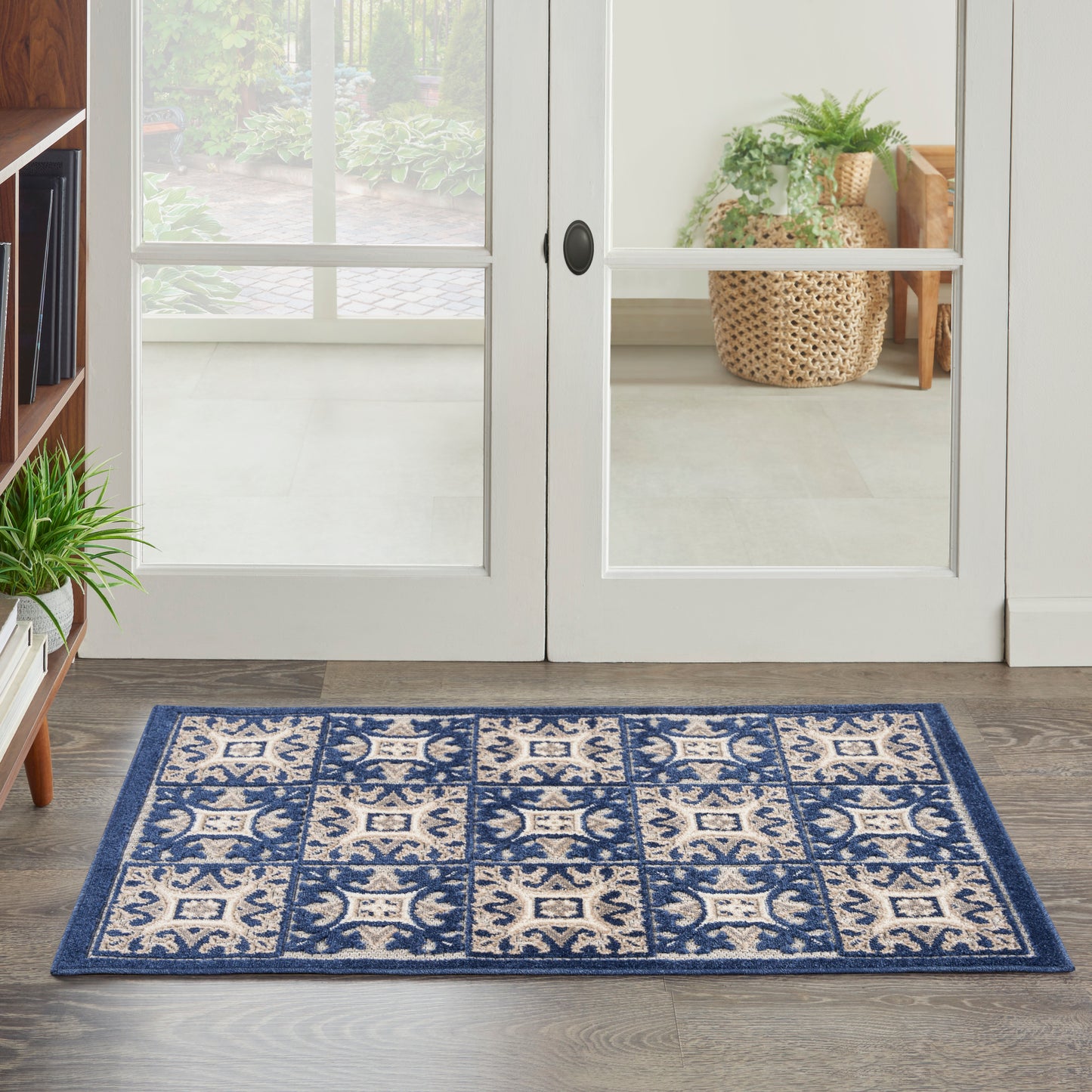 Rectangular blue and ivory patterned area rug on dark wood floor by glass double doors; indoor entry with plants.