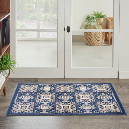 Rectangular blue and ivory patterned area rug on dark wood floor by glass double doors; indoor entry with plants.