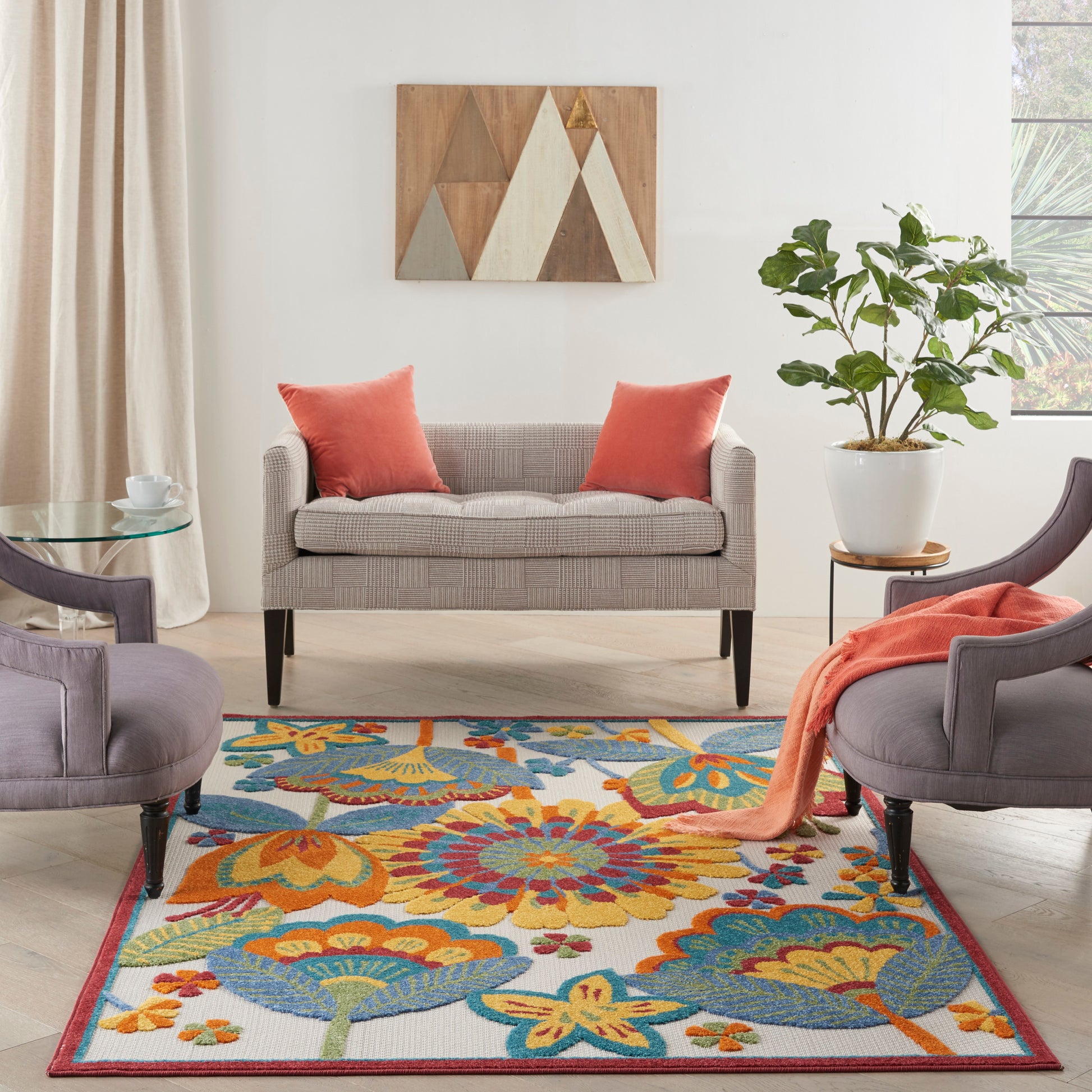 Living room with a gray striped sofa, orange pillows, a colorful floral rug, purple accent chairs, and a potted plant.