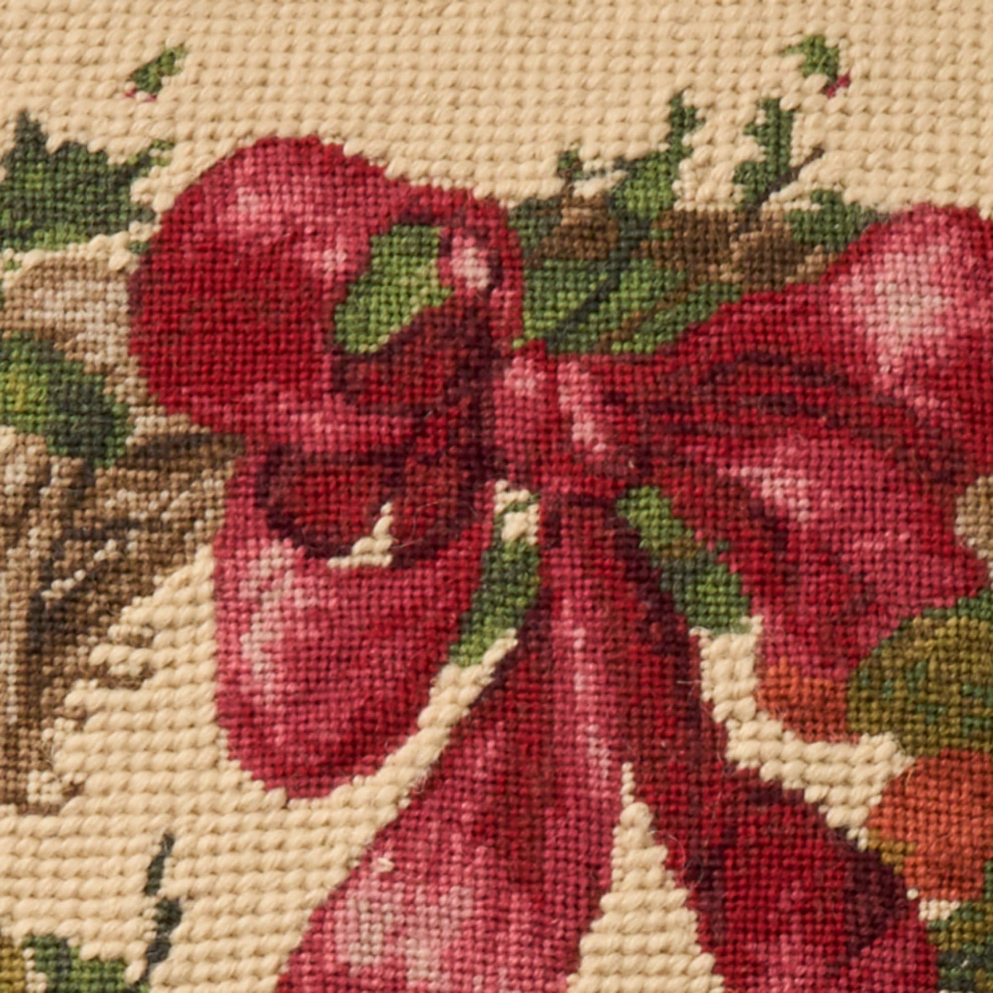 Beige woven rug with a large red bow cross-stitched motif, green leaves; festive holiday design.