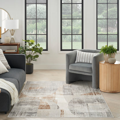 Gray velvet sofa with rounded armchair, striped pillow, beige-gray rug, light wood floor, plants, round wooden side table.