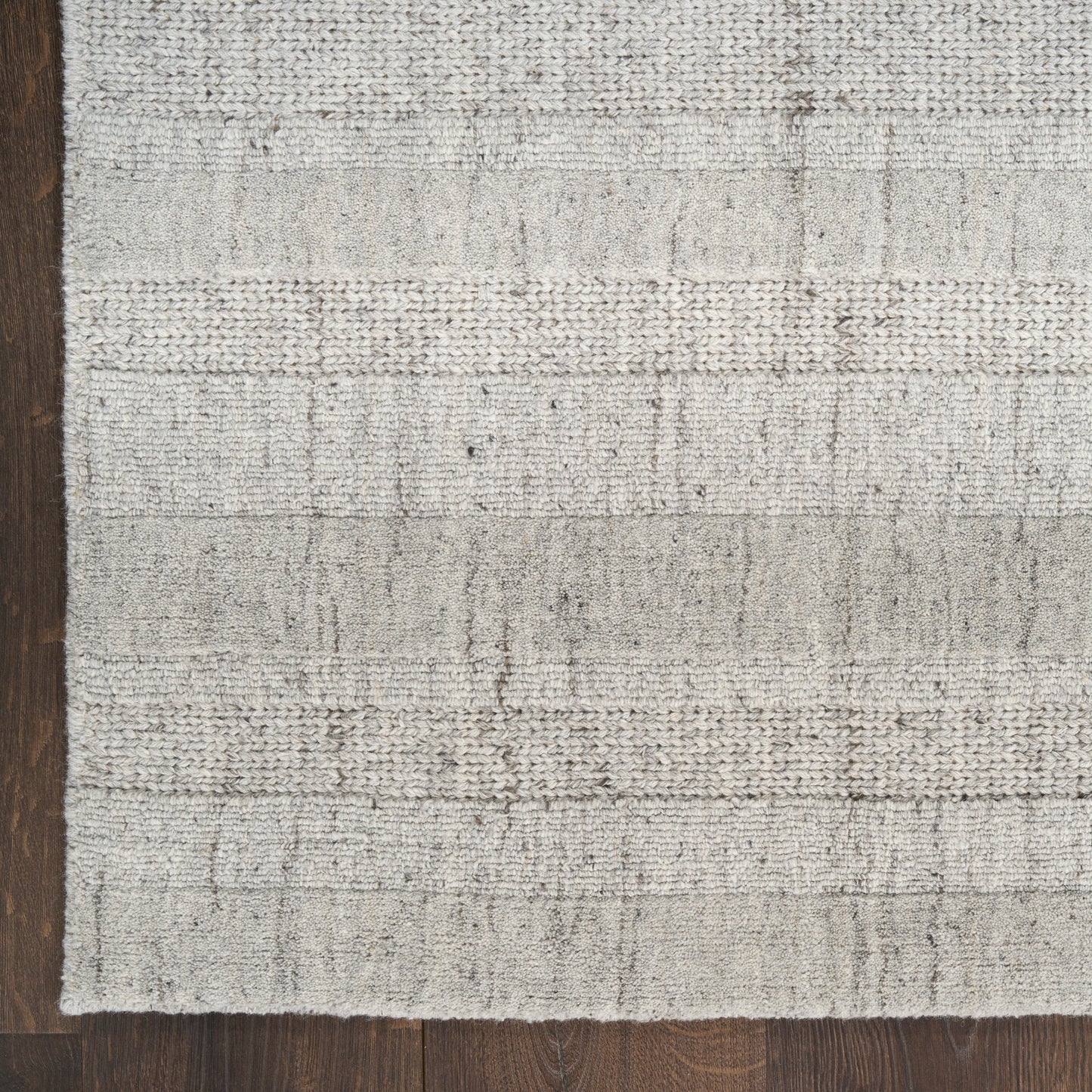 Rectangular light gray textured woven rug with subtle horizontal bands on dark wood floor; modern minimalist style.