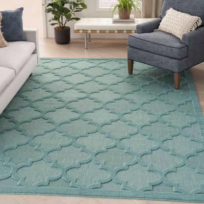 Teal seafoam area rug with trellis/quatrefoil pattern in a modern living room with gray sofa and blue armchair.