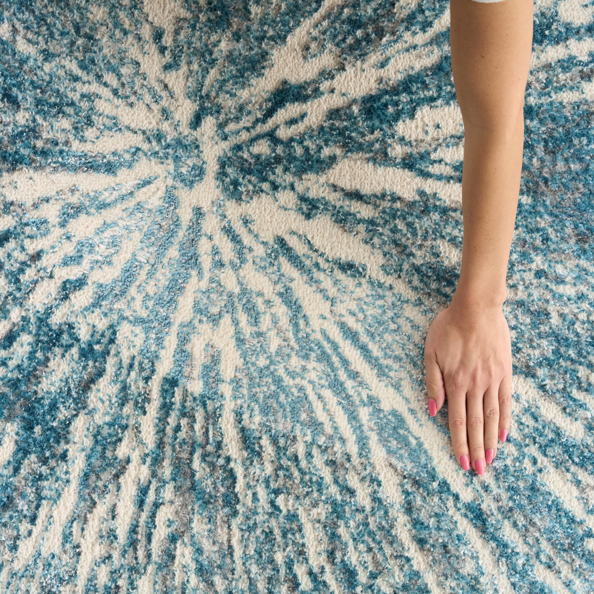 Arm with pink nail polish resting on a blue and cream tie-dye rug.