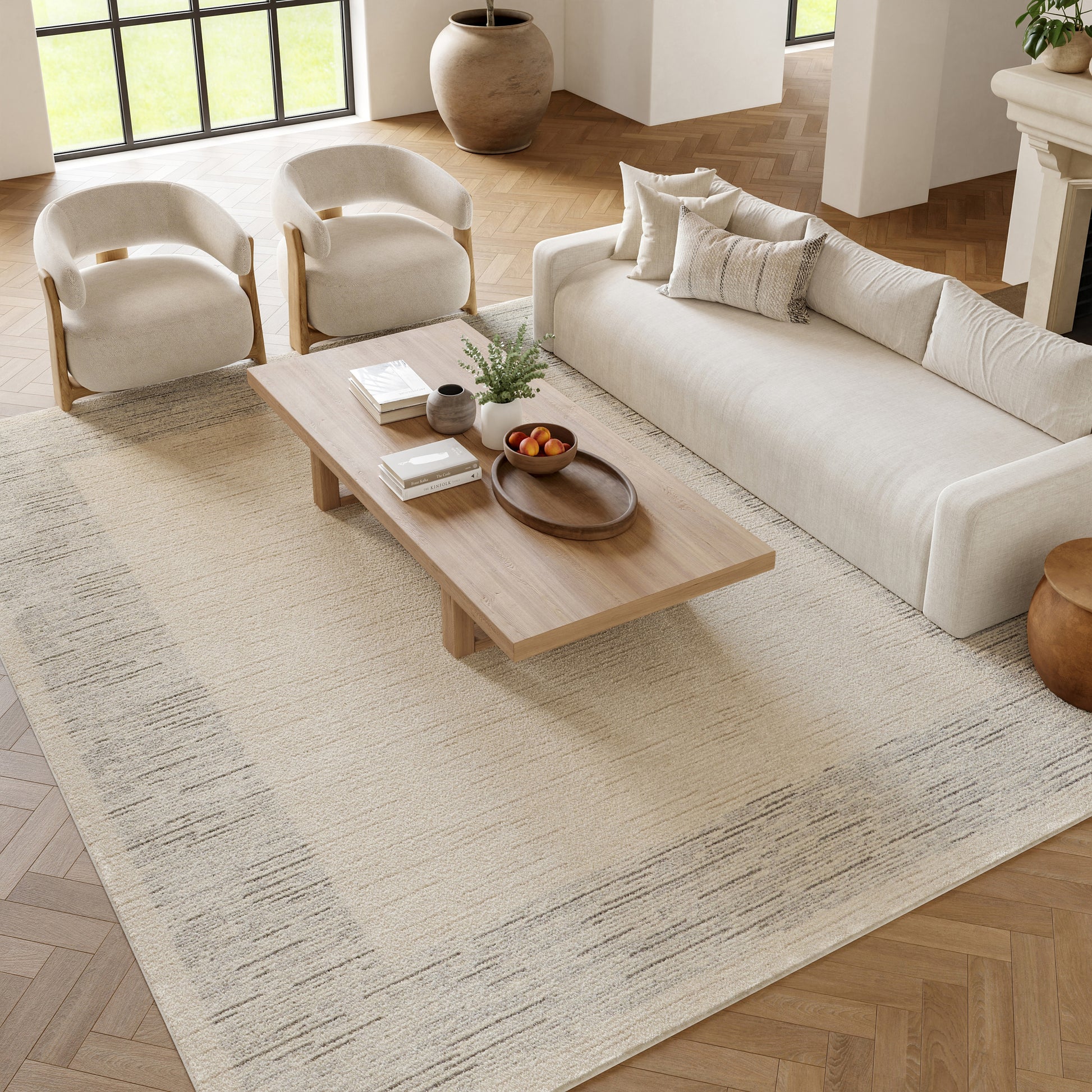 Neutral living room with cream sofa, two armchairs, wooden coffee table, beige patterned rug.