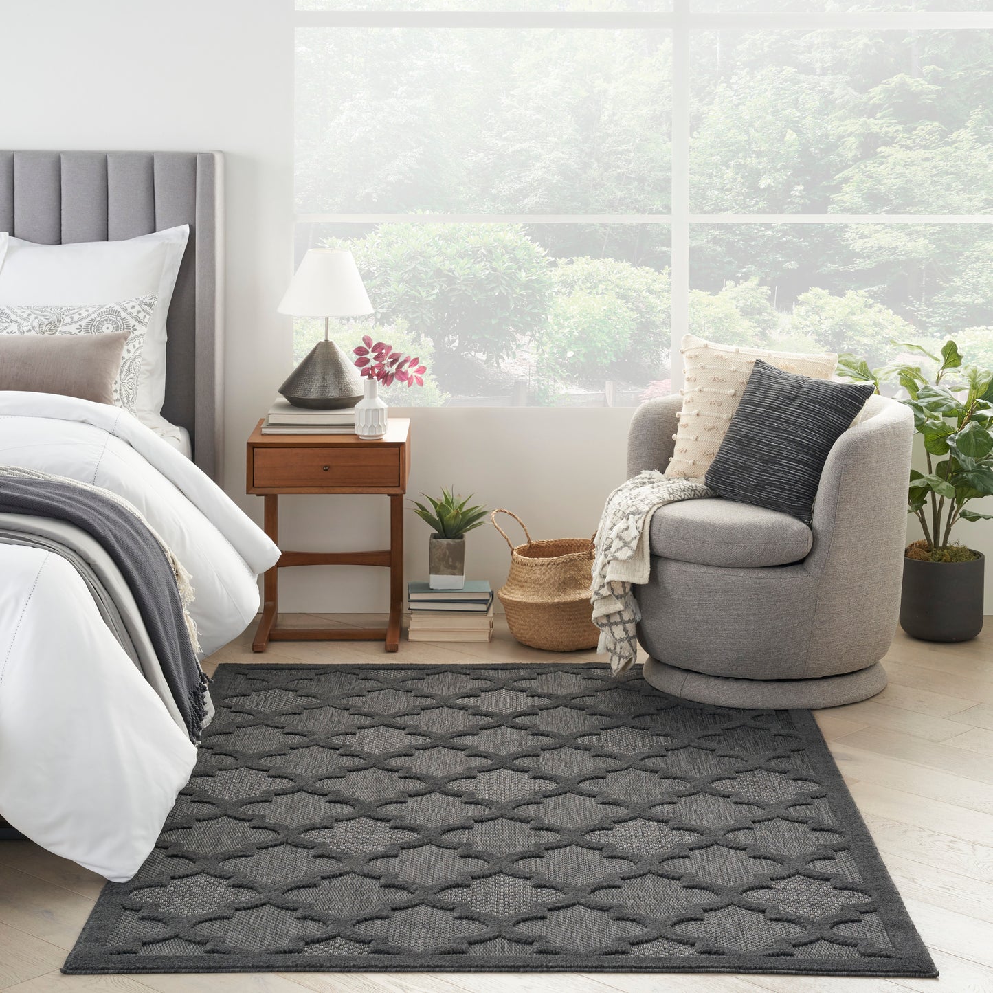 Dark gray woven rug with a repeating geometric pattern on a light wood floor in a bright bedroom.