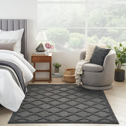 Dark gray woven rug with a repeating geometric pattern on a light wood floor in a bright bedroom.