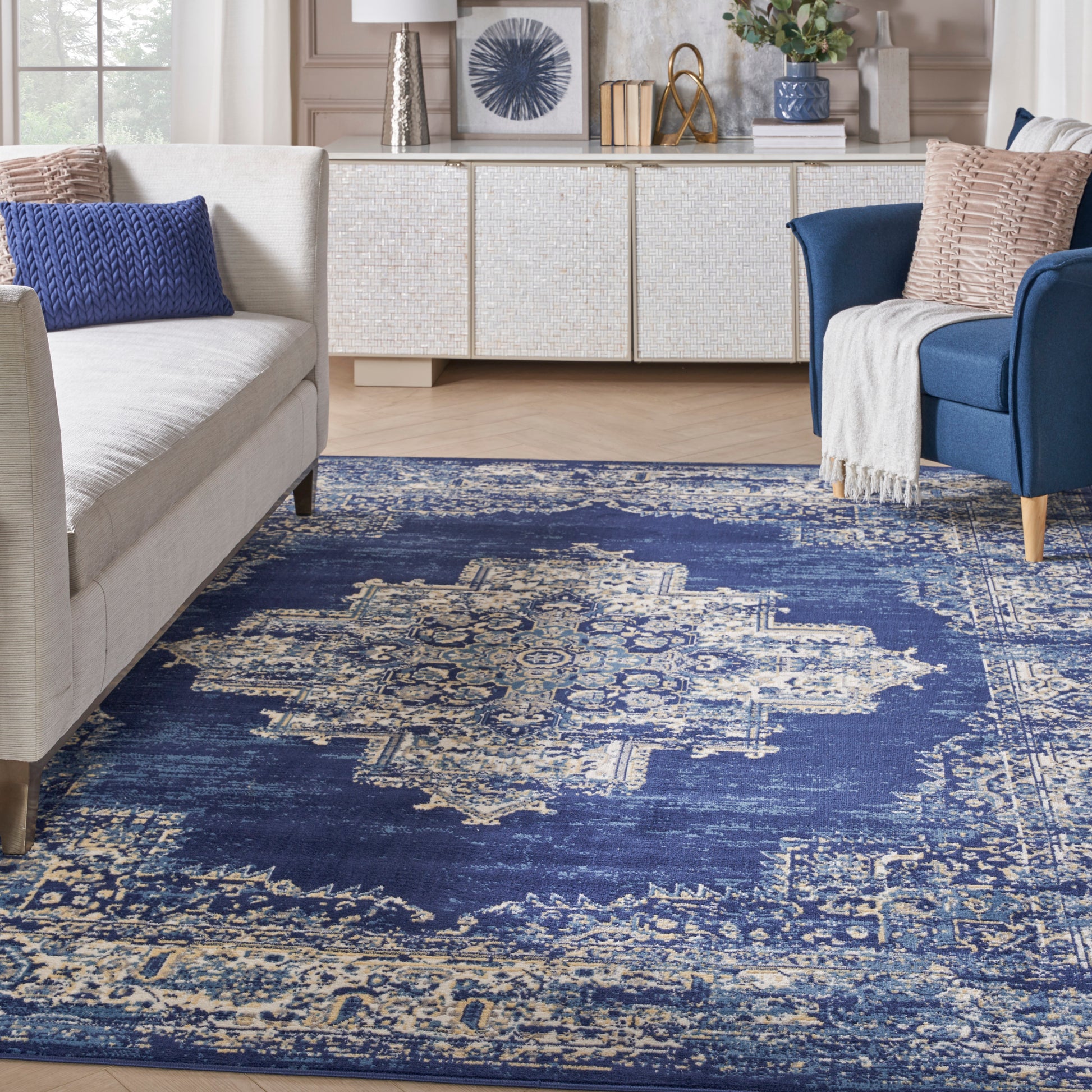 Rectangular indigo blue Oriental area rug with ivory geometric motifs, in a cozy living room with cream sofa and blue chair.