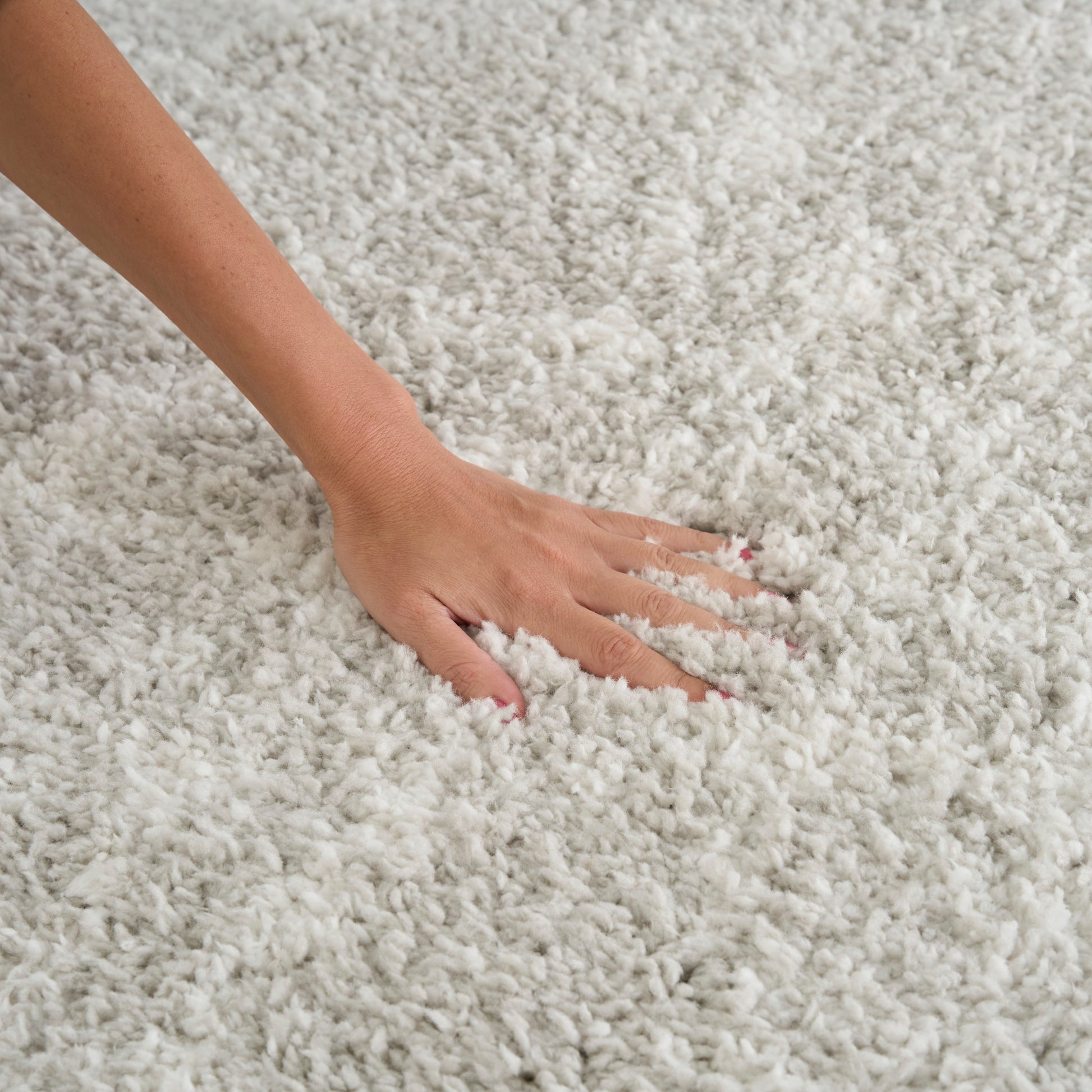 Close-up of a hand pressing into a plush cream shag rug, highlighting soft, fluffy fibers and cozy home décor.