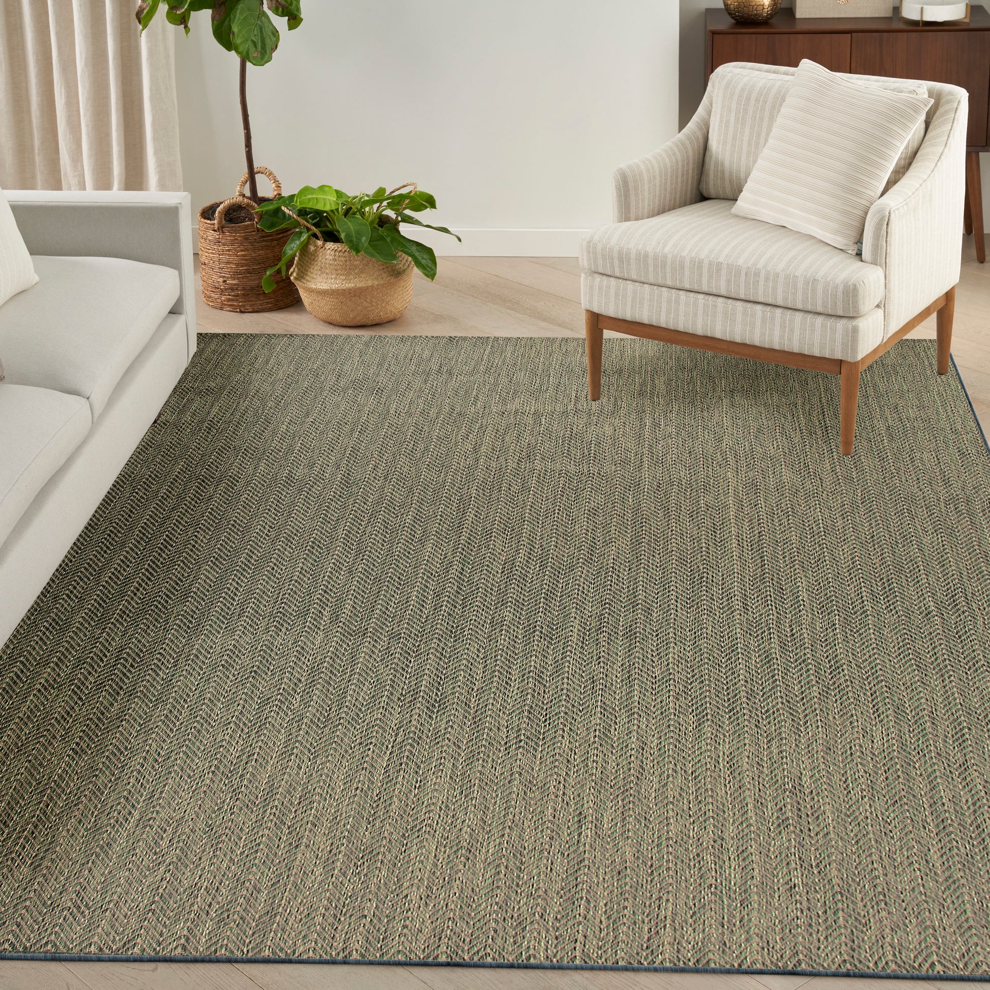 Olive-green textured area rug in a modern living room with cream upholstered chair, light-wood legs, and potted plants.