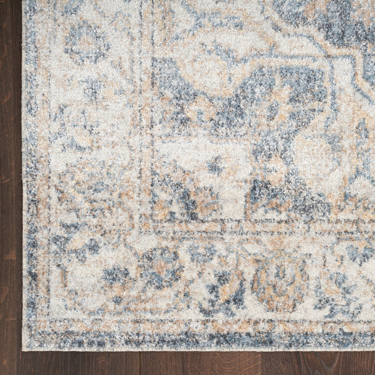 Blue and cream distressed oriental woven area rug on dark wood floor, showing ornate border and floral motifs.