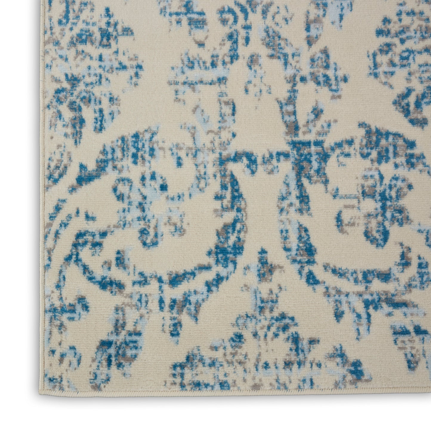 Beige rug with blue distressed damask pattern, woven textile floor covering.