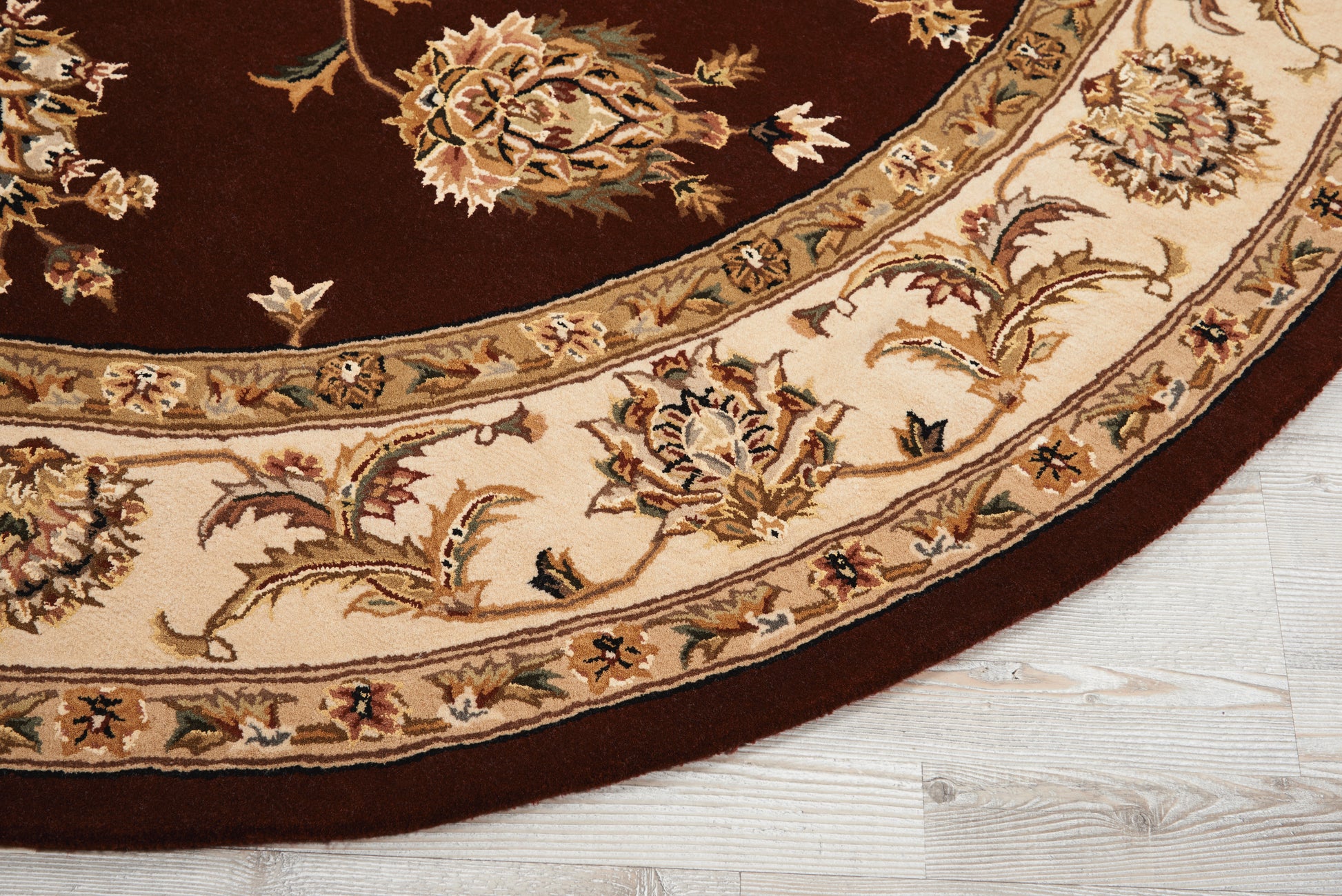 Round oriental rug with burgundy center and cream floral border, intricate vine motifs; wood floor visible.