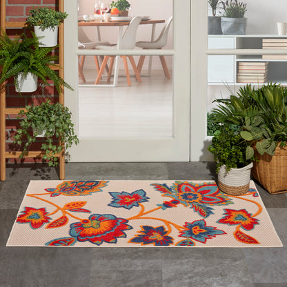 Rectangular beige rug at doorway with a bright orange, red and blue floral pattern, surrounded by potted plants.