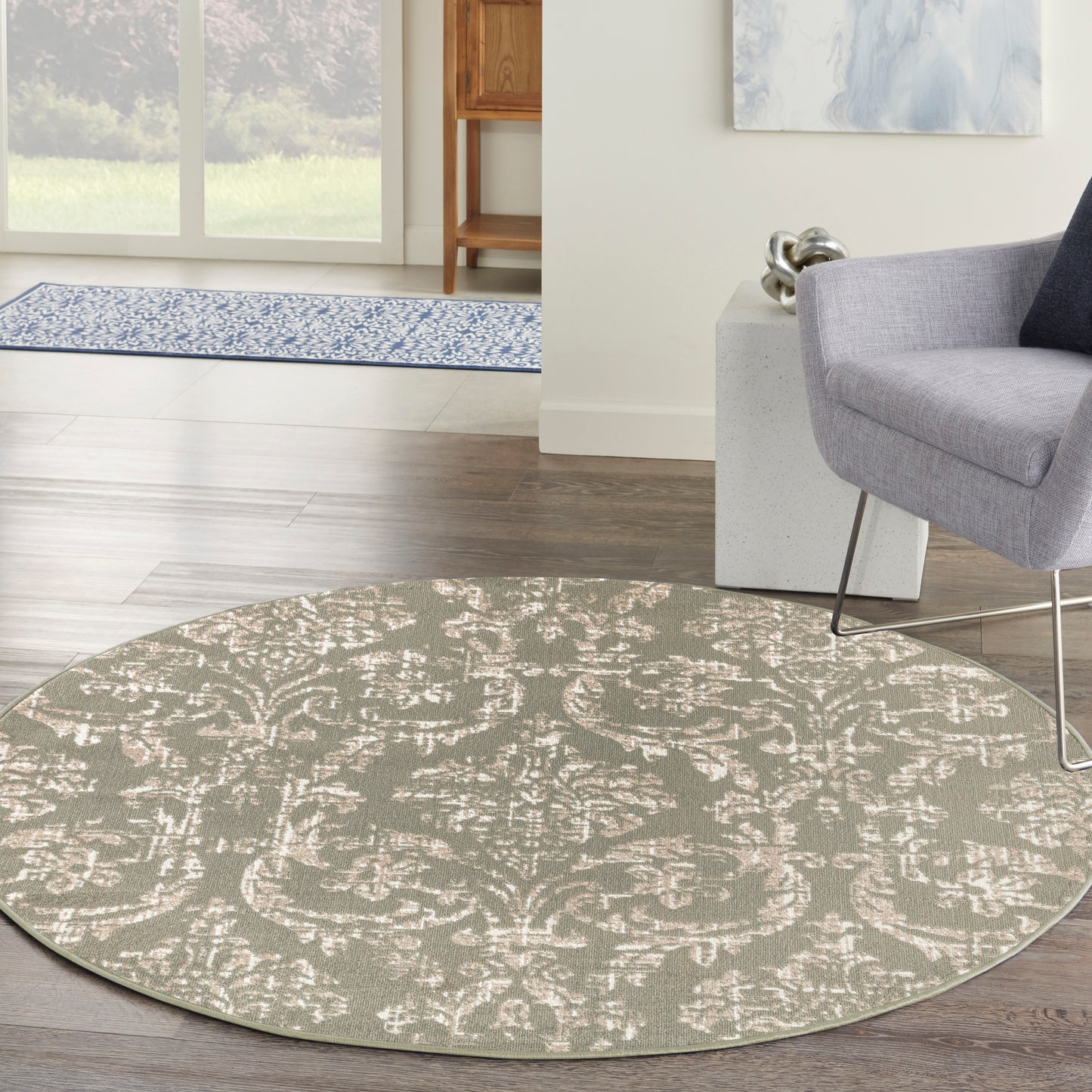 Round taupe rug with cream damask pattern; soft plush texture in a modern living room beside a gray chair.