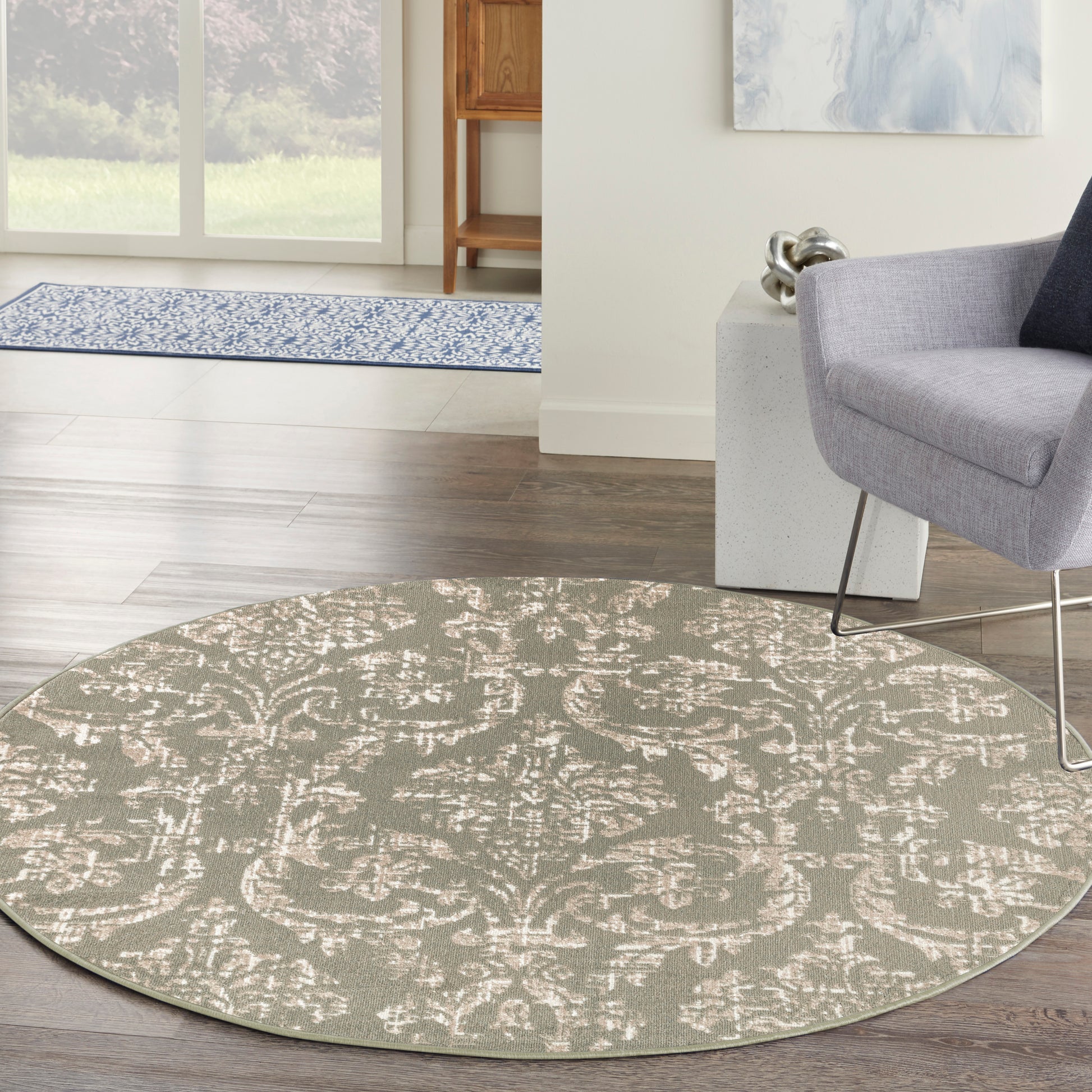 Round taupe rug with cream damask pattern; soft plush texture in a modern living room beside a gray chair.