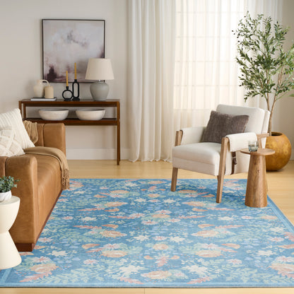 Cozy living room featuring a blue floral rug, tan leather sofa, white armchair, wooden console table, and a leafy plant.