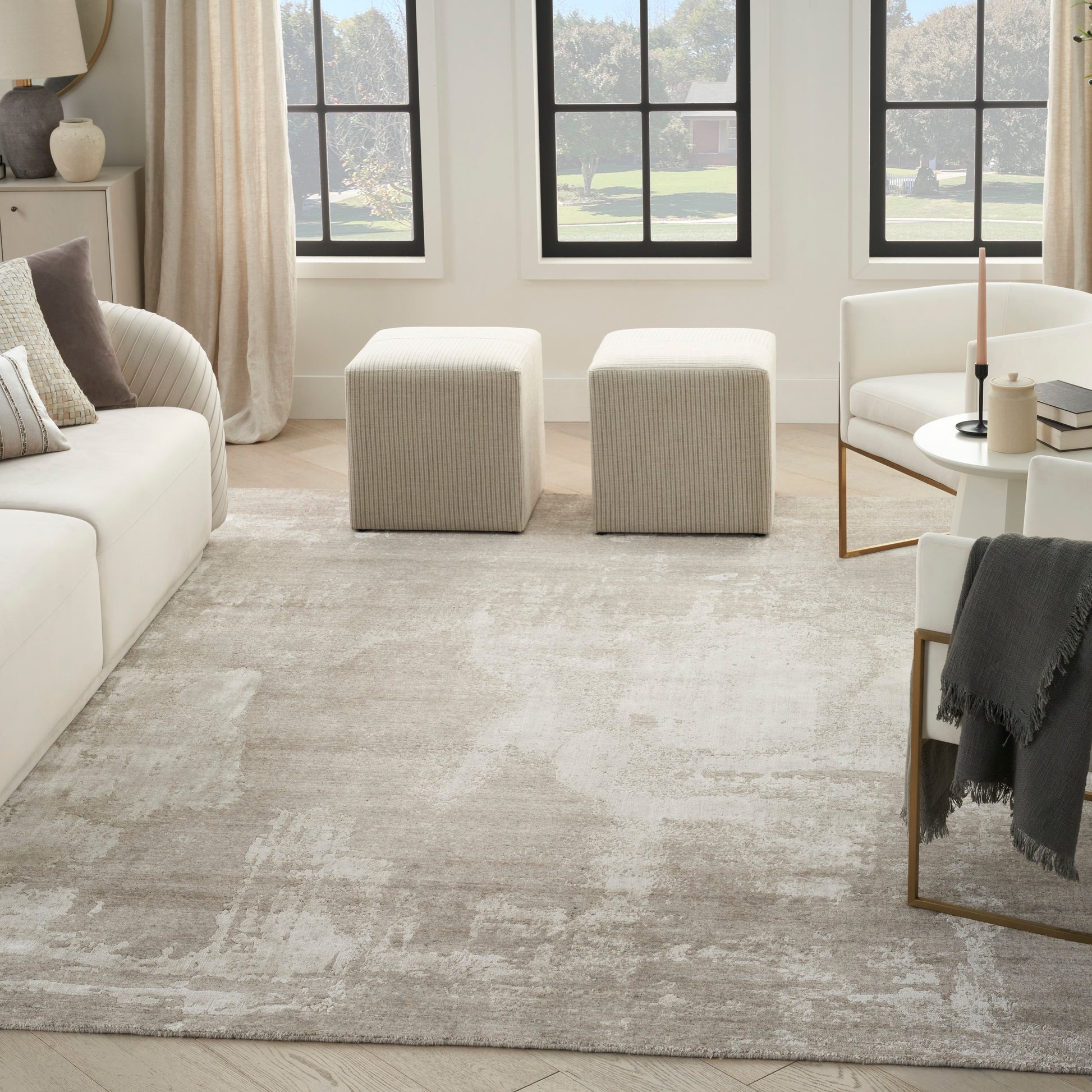 Beige textured area rug in a bright modern living room with cream sofa, two square ottomans, and white chairs.